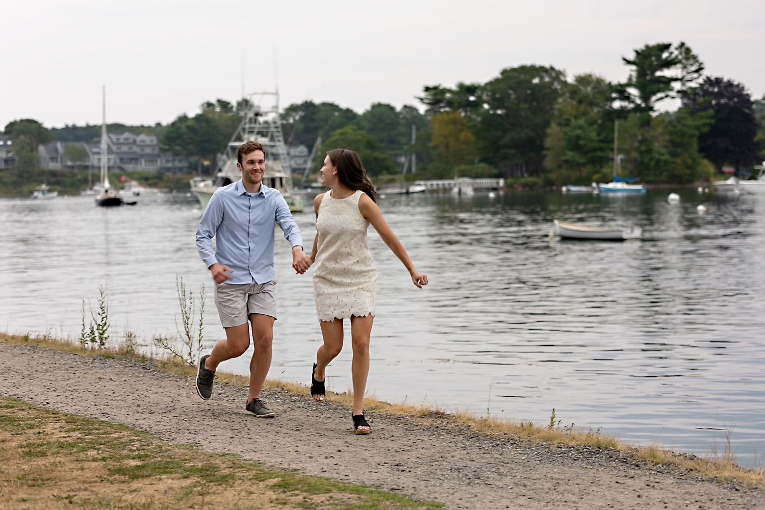 A couple walks hand in hand along a waterfront path with multiple scenic views of the shoreline.
