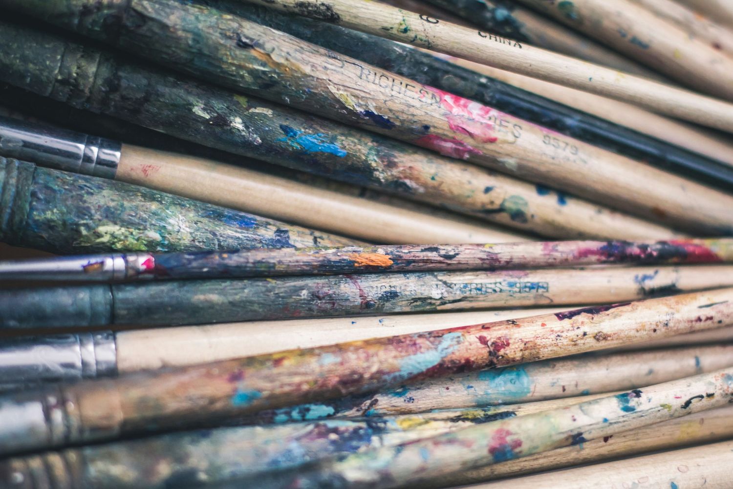 Close-up view of used paint brushes with colorful dried paint residue arranged diagonally across the frame.