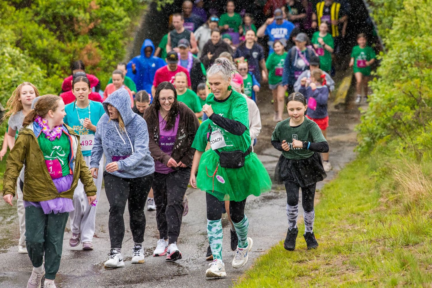 Large group of participants walking along a path in a charity fun run event, wearing colorful outfits on a cloudy day.