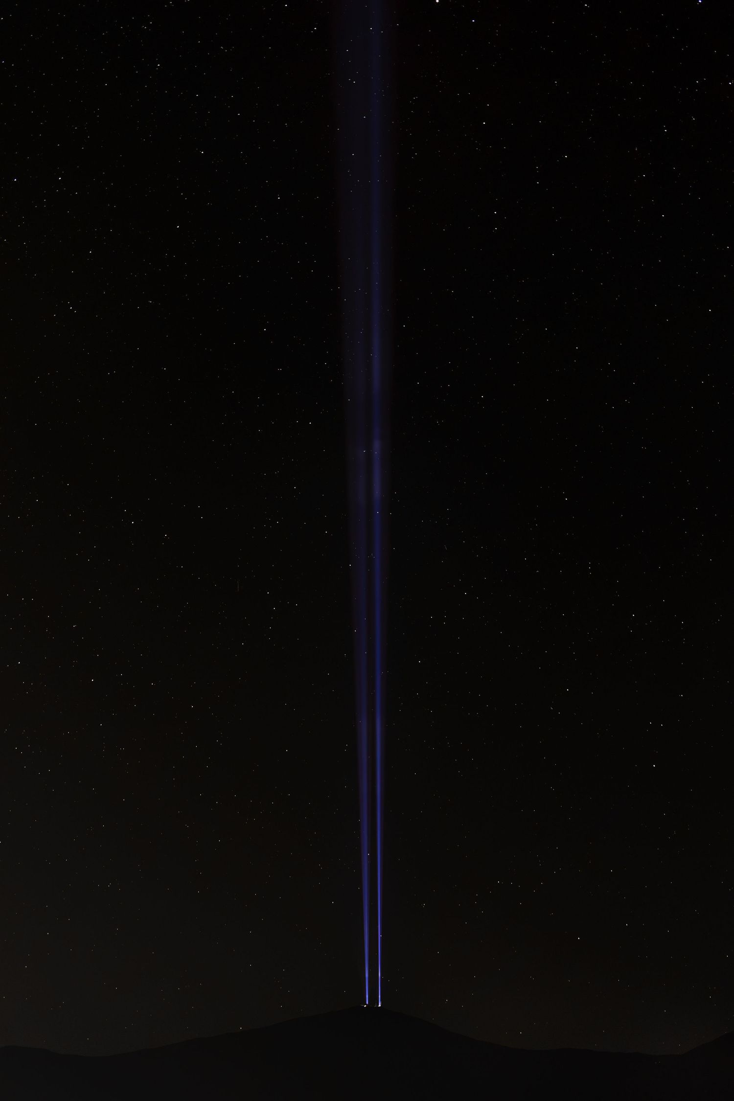 A single beam of blue light shoots upward into a dark starry night sky from a distant horizon.