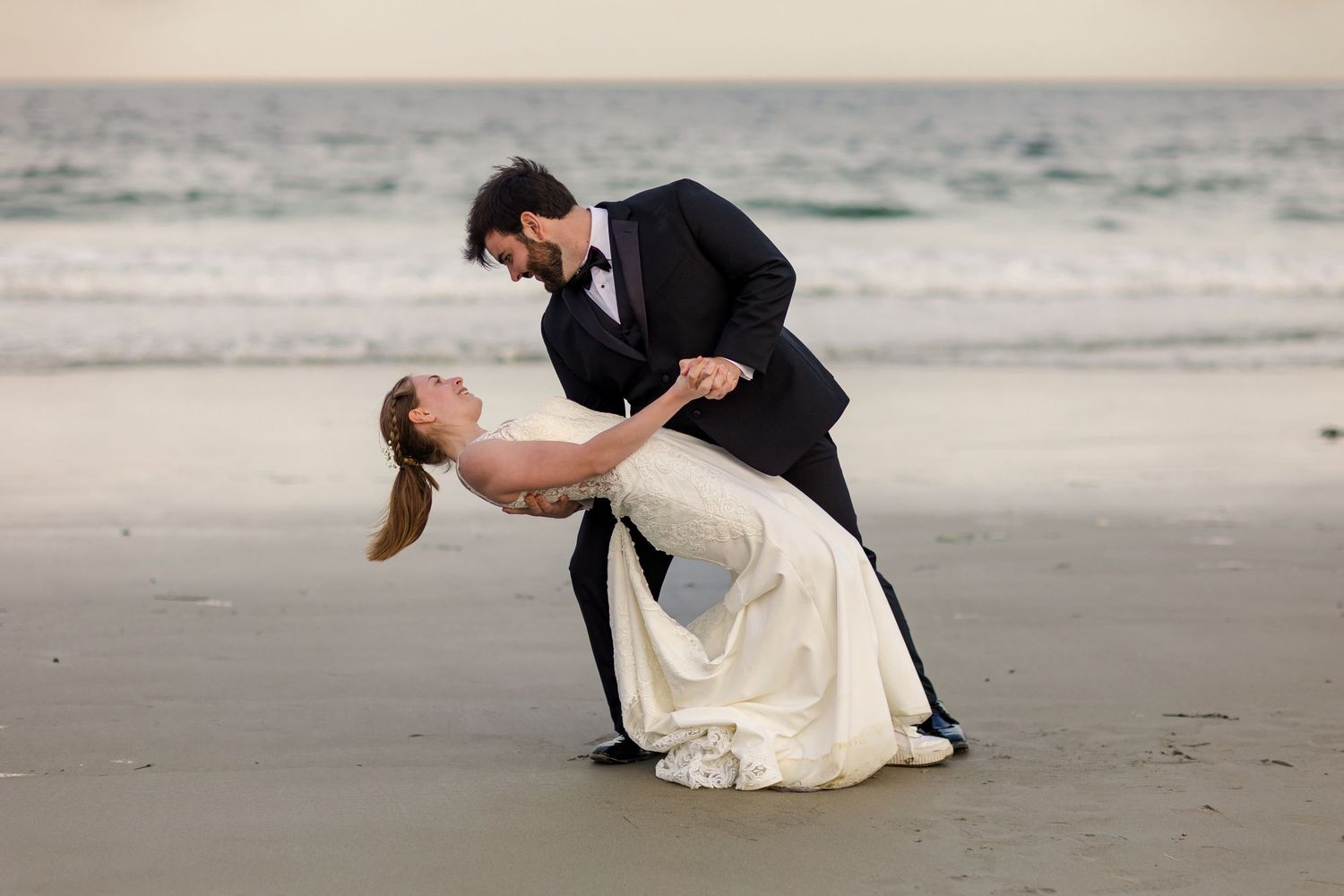 A couple in wedding attire dances romantically on Mother's Beach in Kennebunk, Maine at sunset.