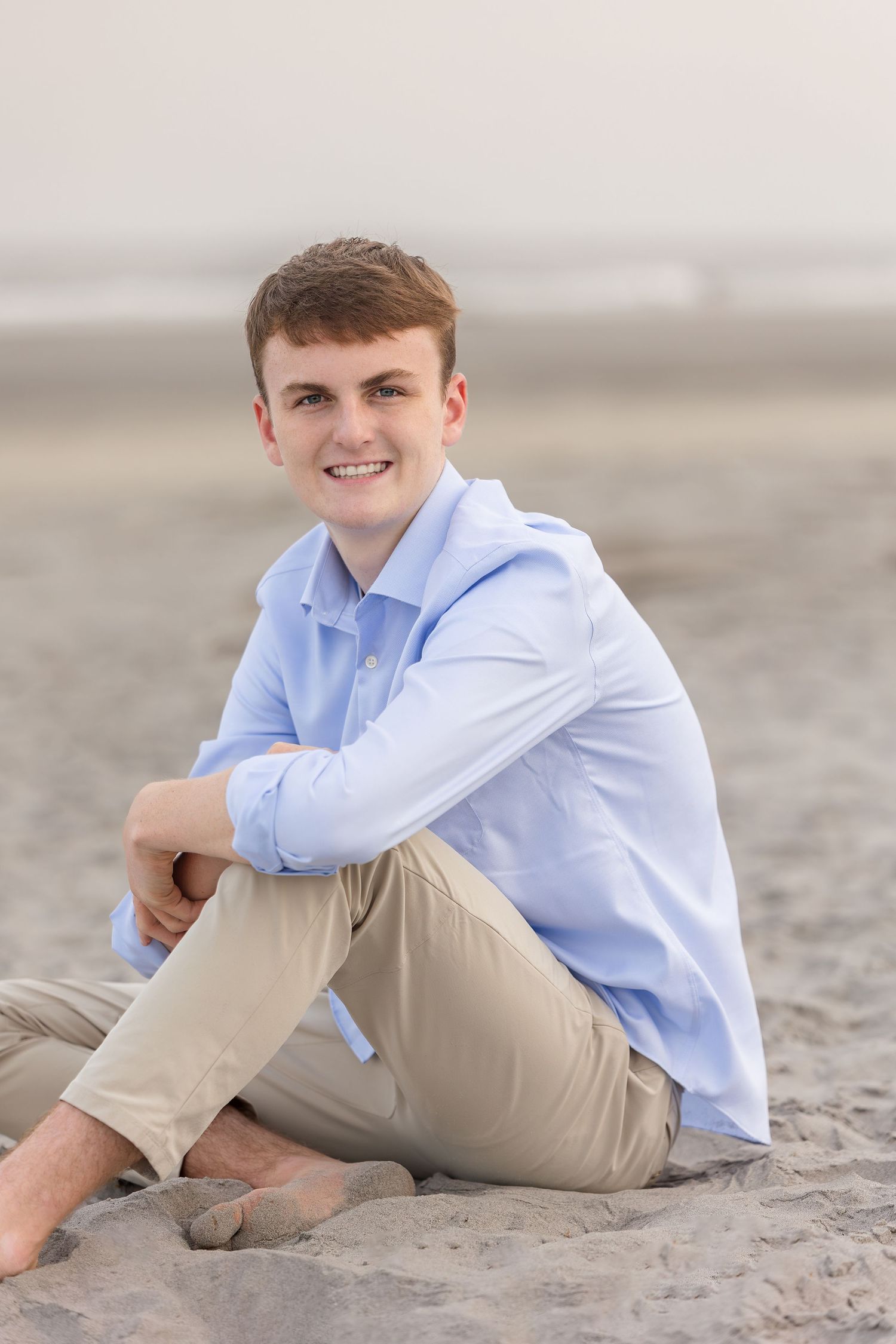 A series of beach portraits showing a graduating senior in a light blue button-down shirt and khaki pants relaxing on sandy shore.
