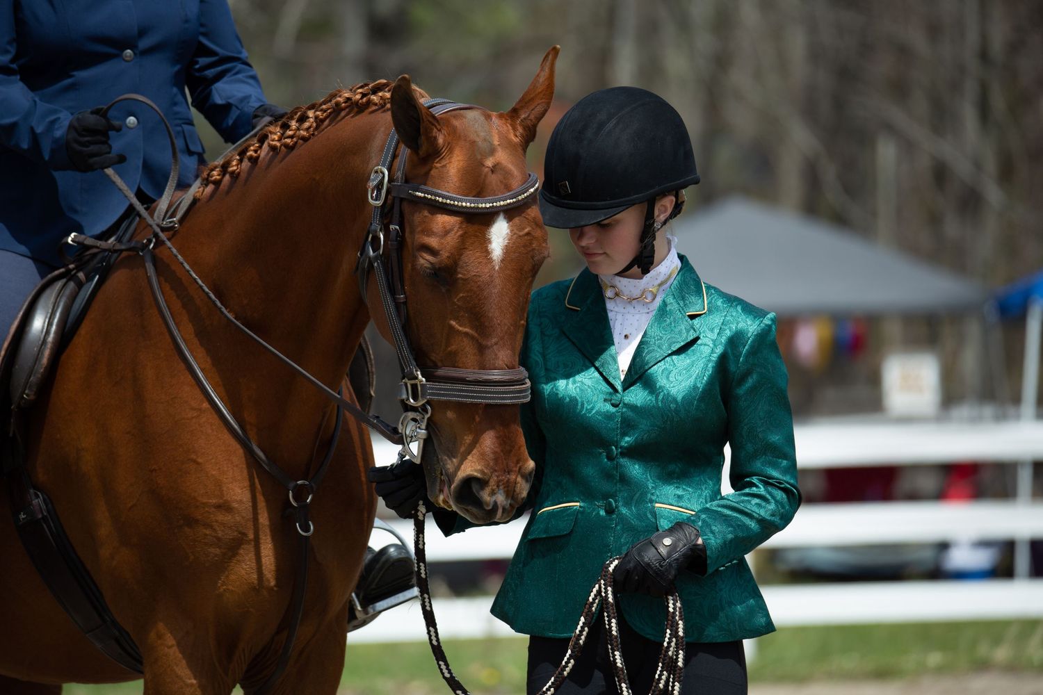 Equestrian rider in green jacket competing in dressage competition with chestnut horse.