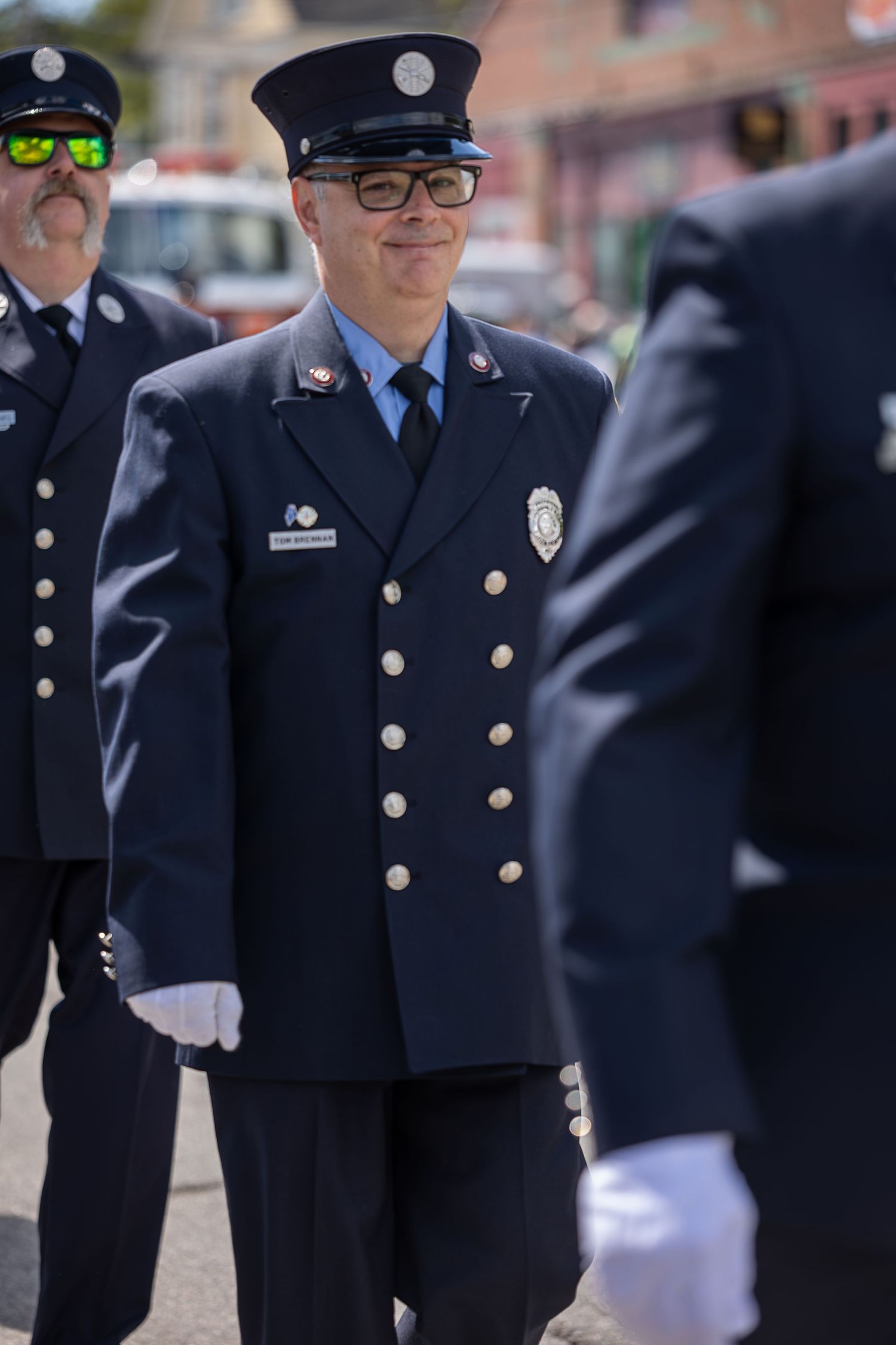 Firefighter in dress uniform with badge and white gloves smiling during a parade ceremony.