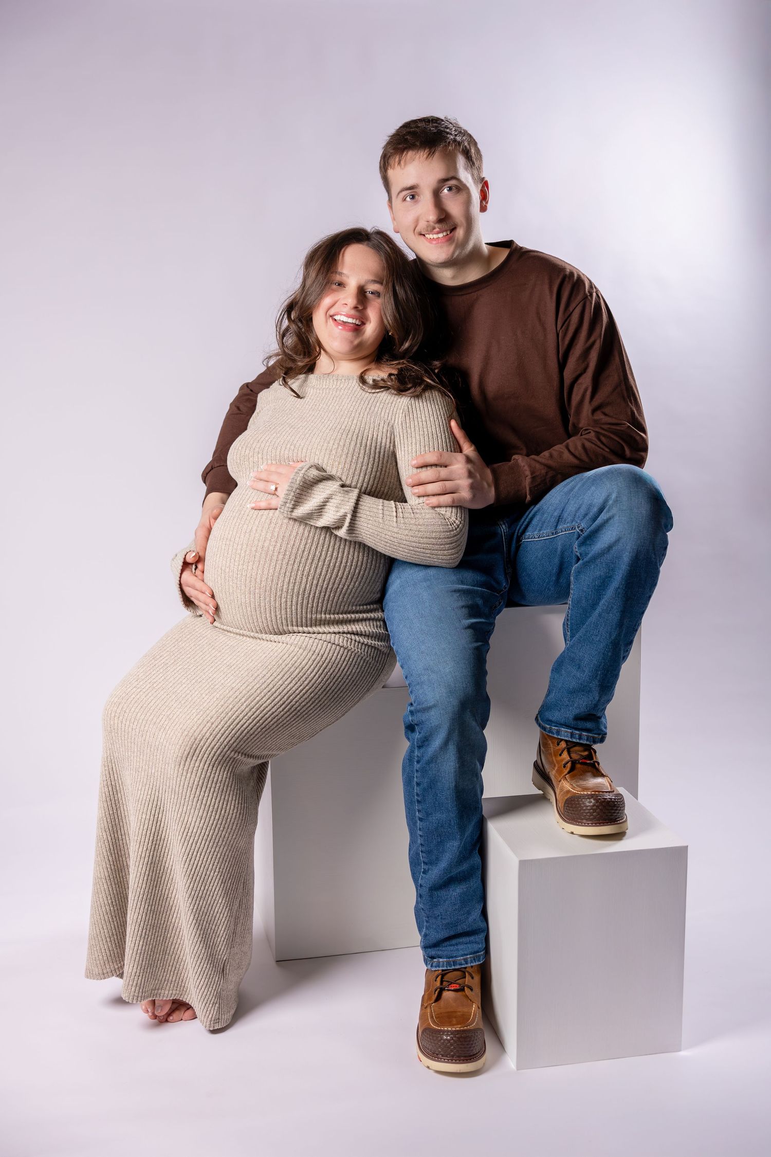 A series of four maternity photos showing a couple posing together on a white backdrop with casual attire.