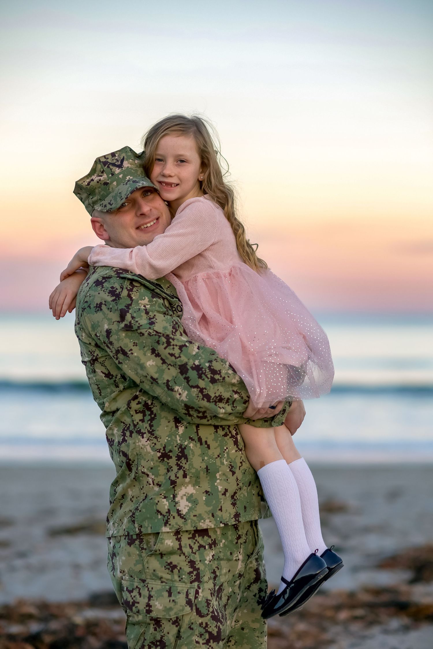Heartwarming embrace on a beach at sunset with military camouflage uniform.