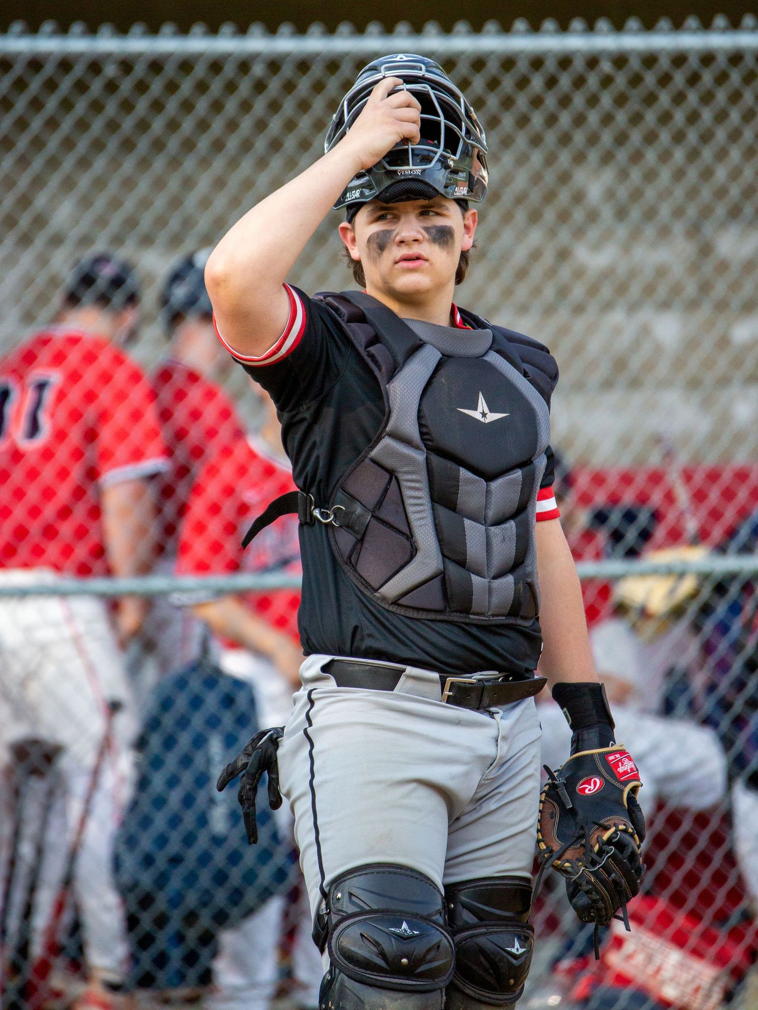 A baseball catcher in protective gear and sunglasses stands ready behind home plate during a game.