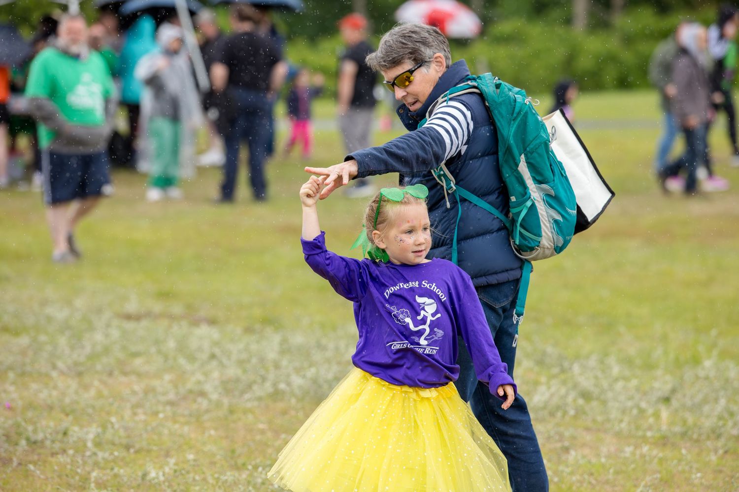 Adult spinning a young girl in a yellow tutu at an outdoor event on a grassy field.