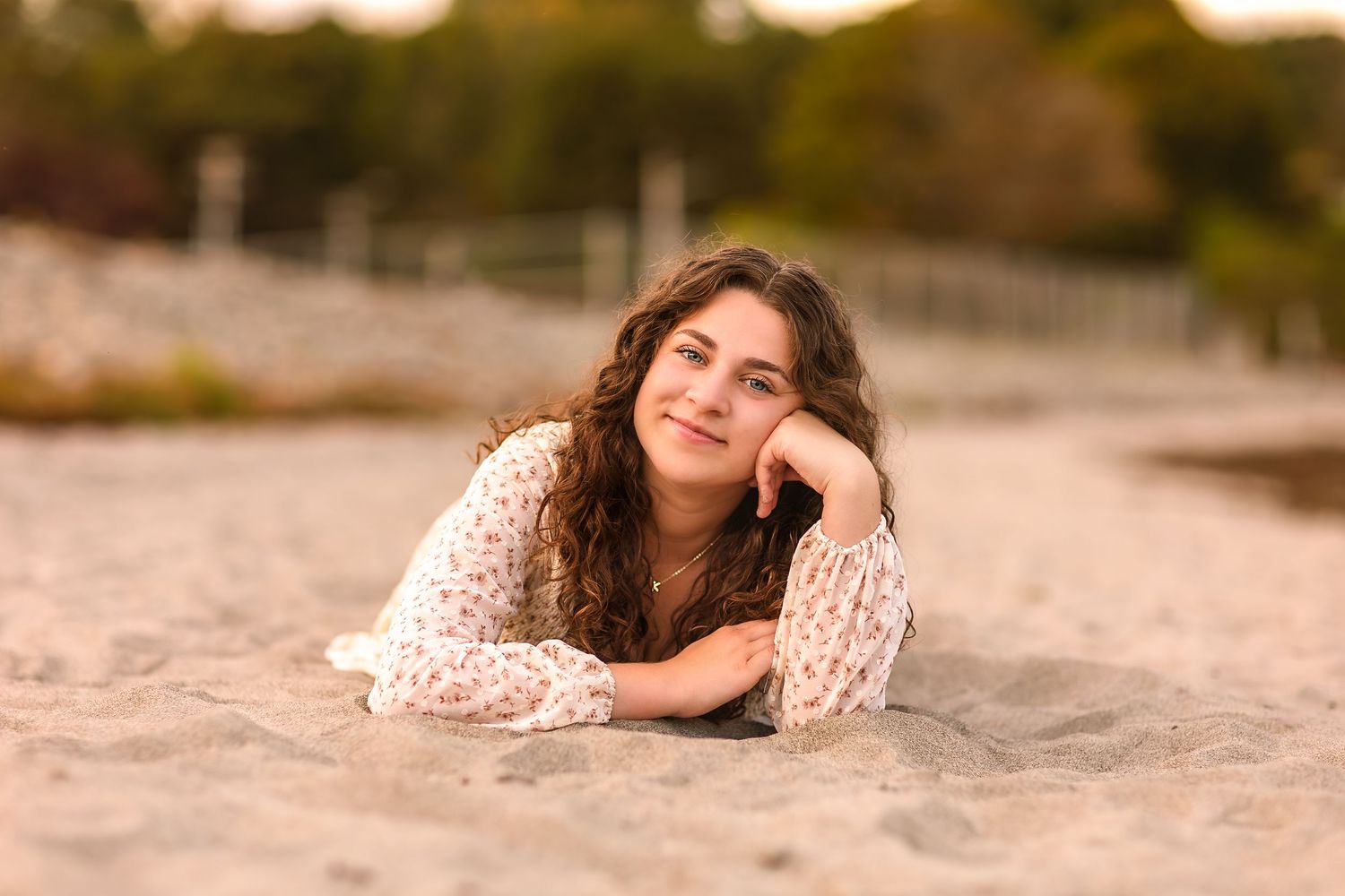 A person in a white lace dress poses on the beach during golden hour sunset with a dreamy expression.