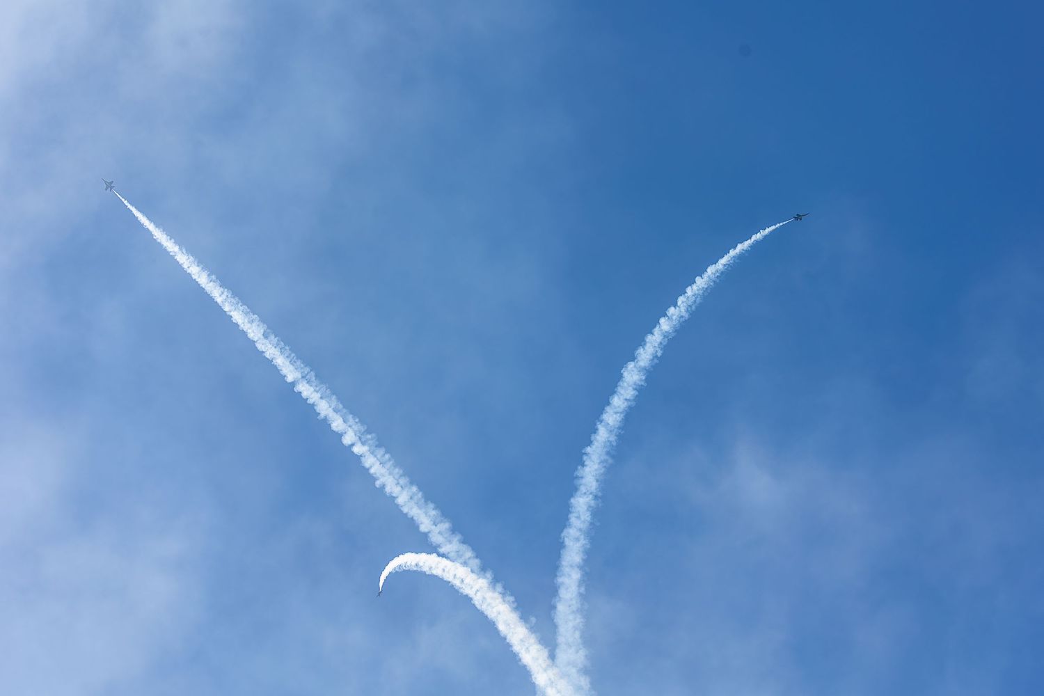 A sequence of contrails from airplanes form parallel white lines across a bright blue sky.