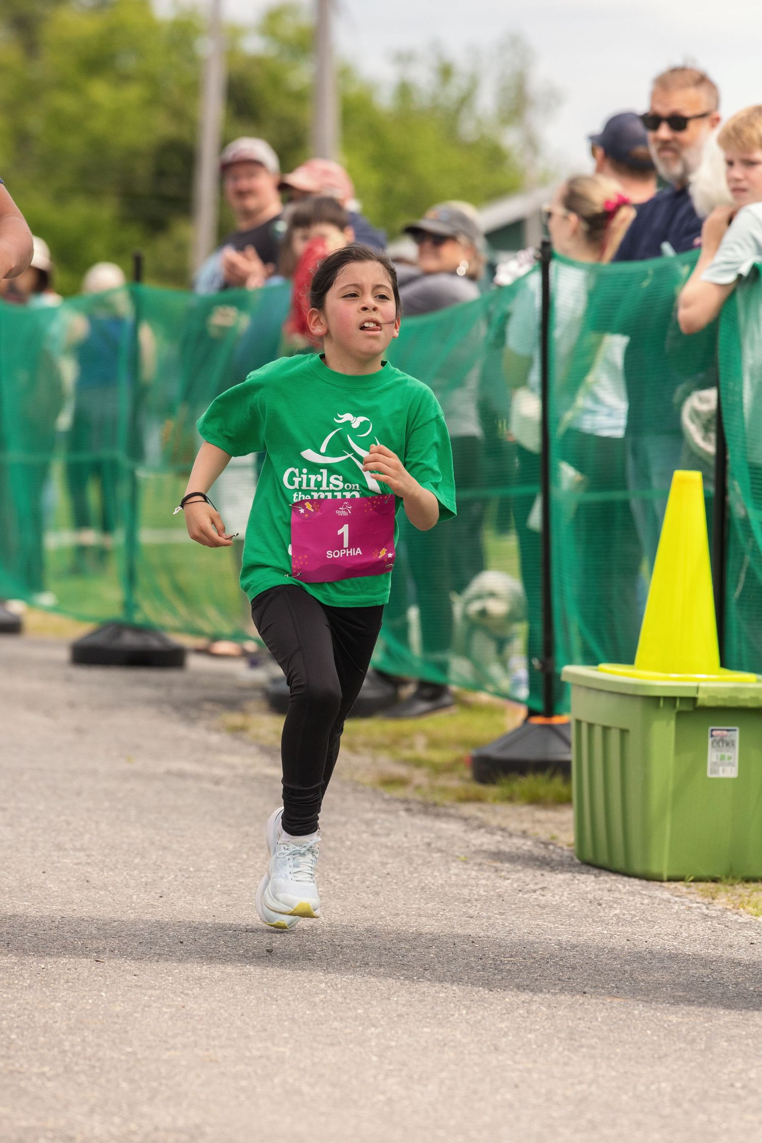 Young girl in green Girls on the Run shirt sprinting toward finish line at a charity race event.