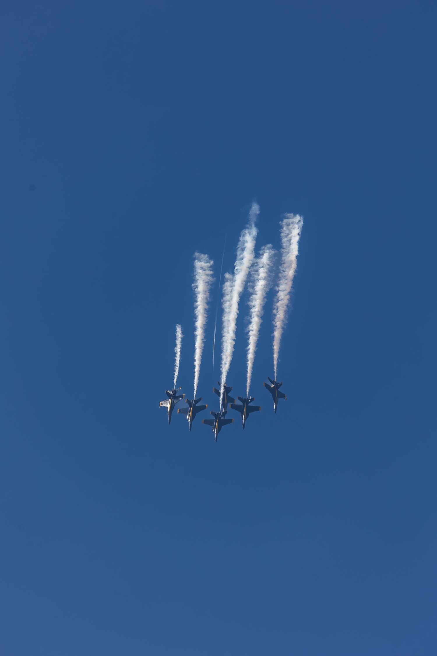 Military jets fly in tight formation with white contrails against deep blue sky during an aerial demonstration.