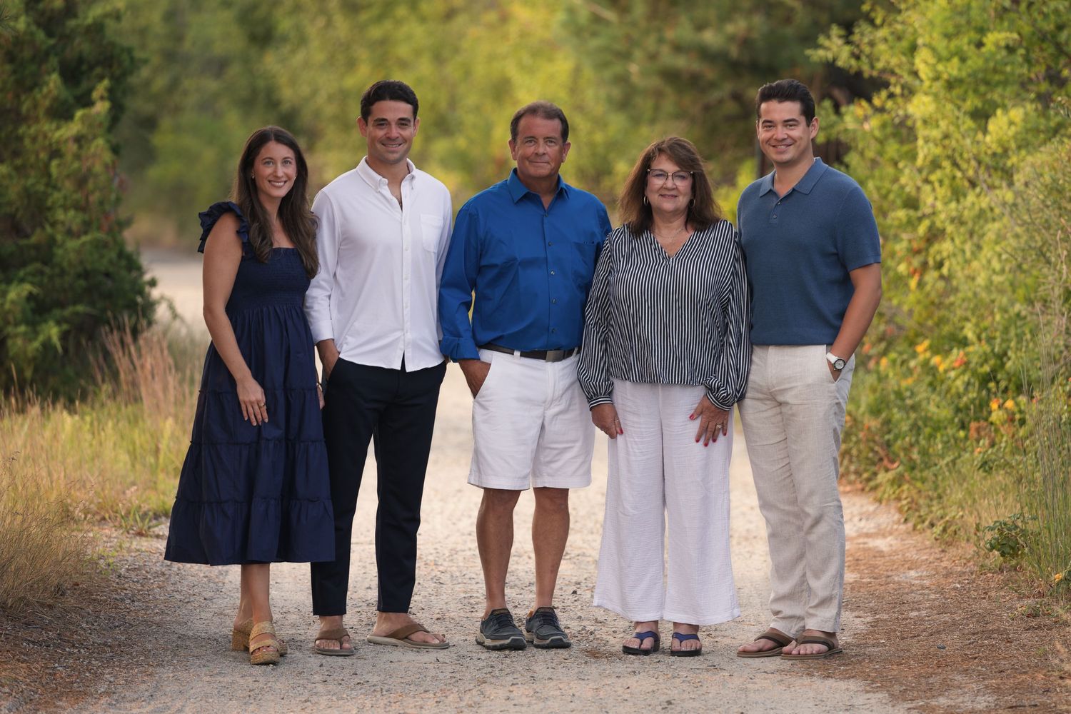 Family of five smiling together on a scenic dirt path surrounded by lush greenery.