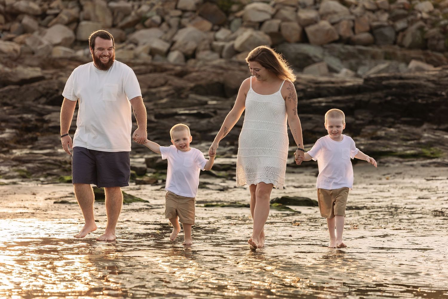 Family walking together on sandy beach with rocky cliffs in background at sunset.