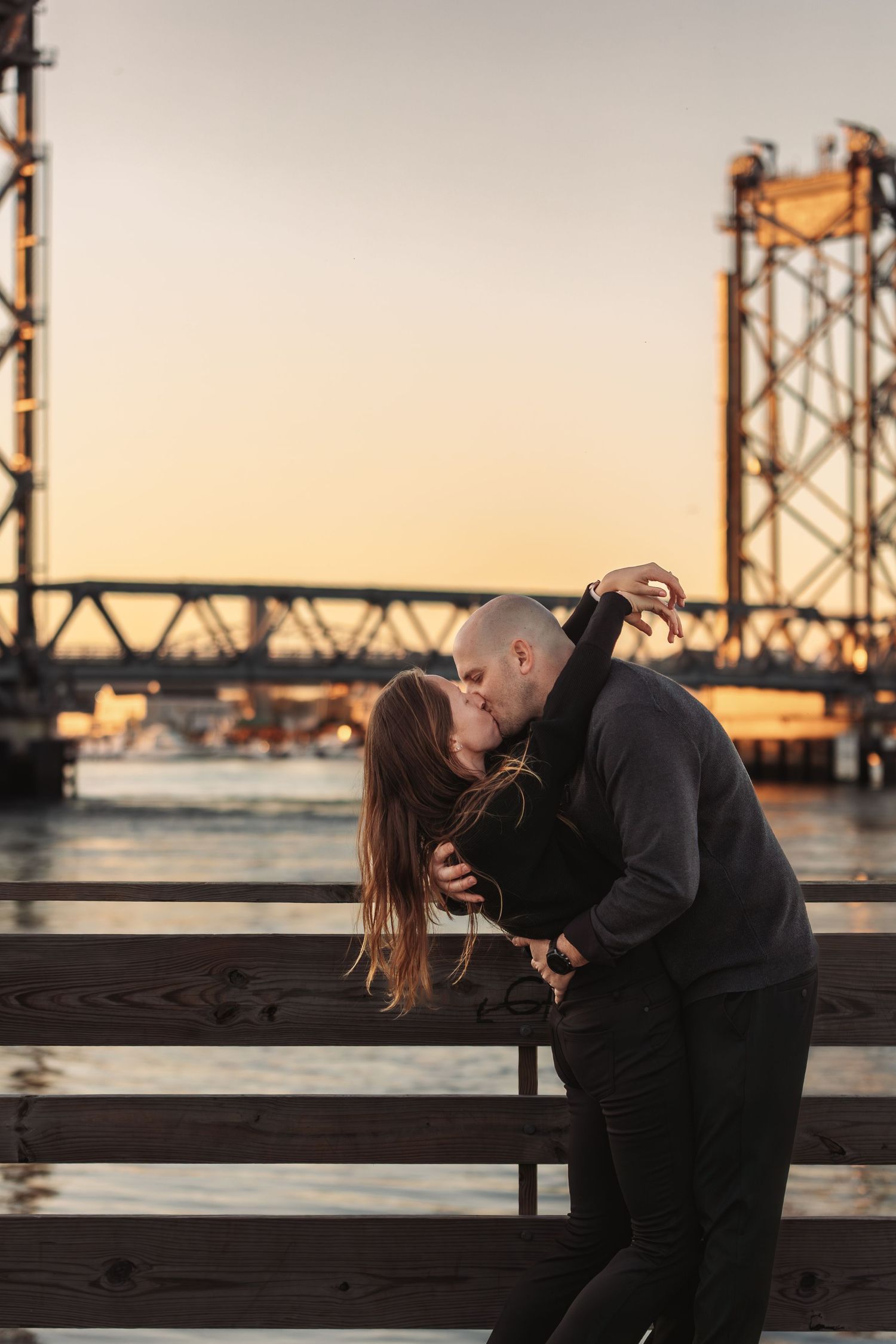 Romantic couple shares intimate moment by industrial waterfront at sunset.