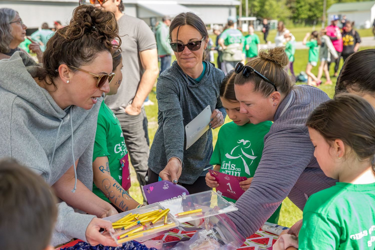 Group of women in green Girls on the Run shirts gather around a table at an outdoor charity event.