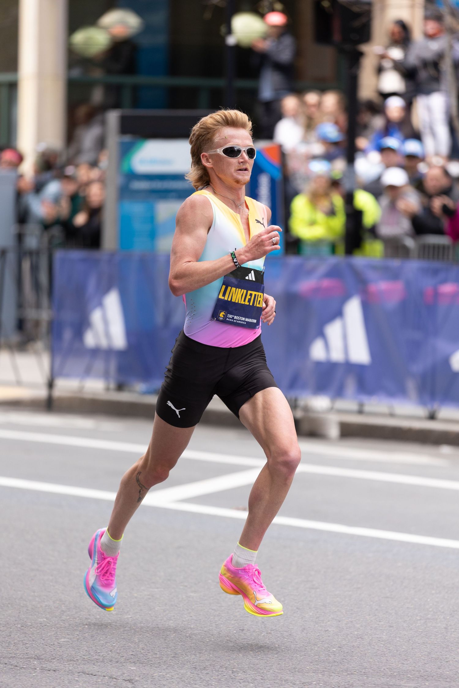 Male marathon runner in Puma gear and pink shoes races through city street during competitive road race event.