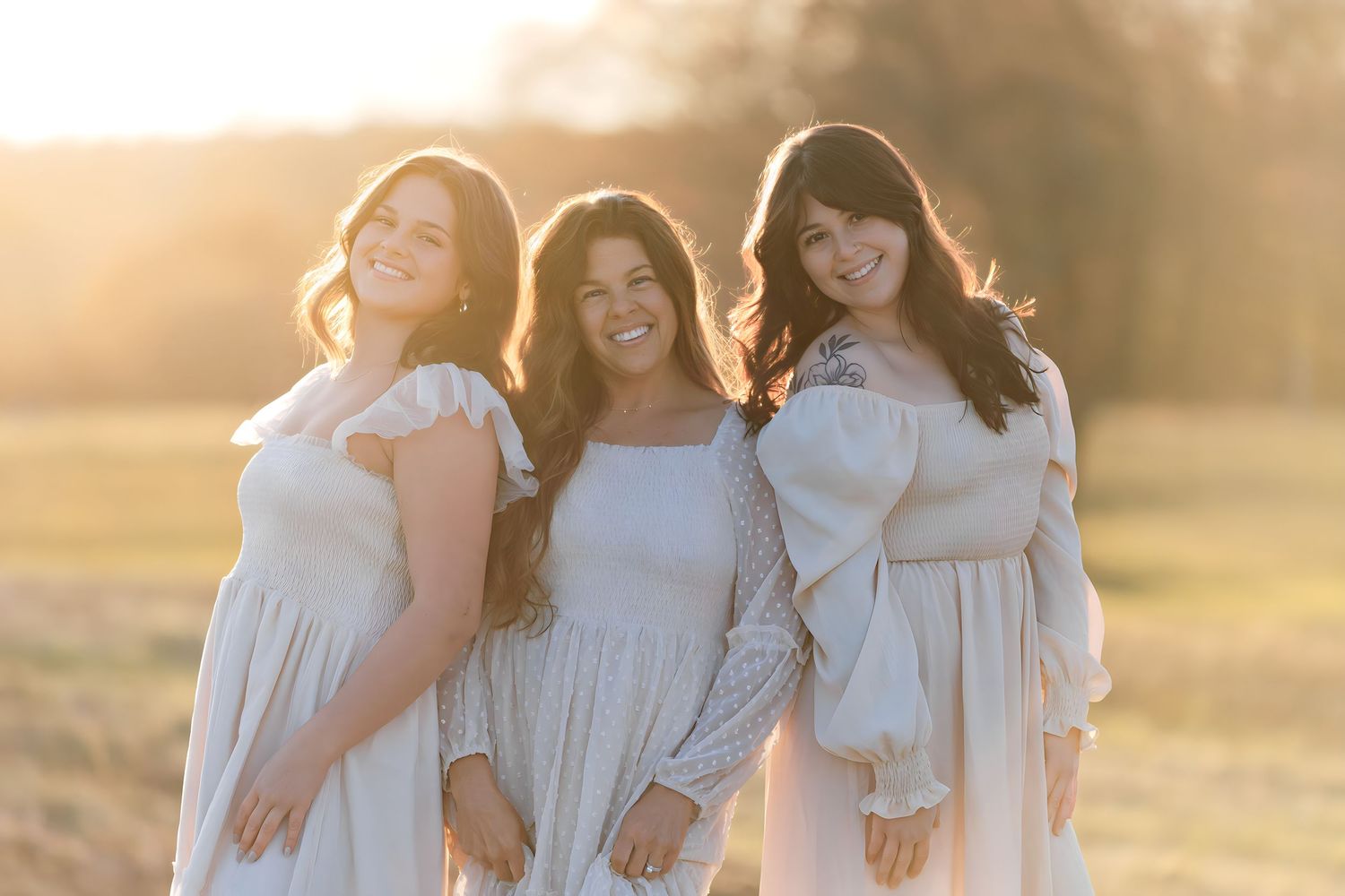 Family wearing white dresses poses together during golden hour sunset in a field.