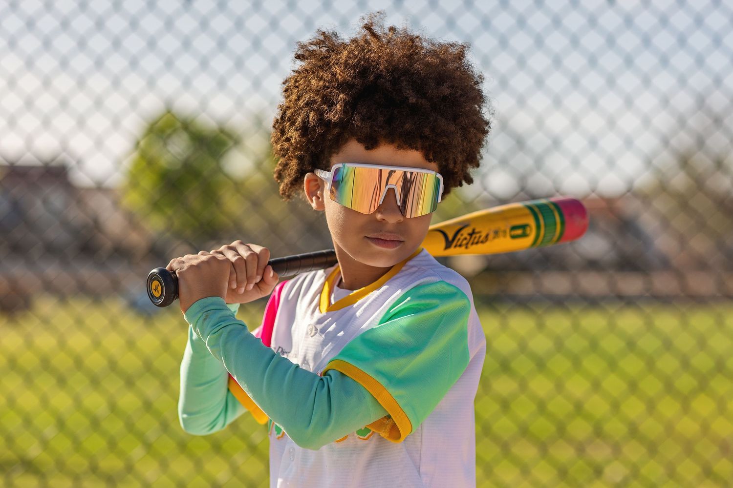 Baseball player in white uniform swinging a colorful bat during practice.