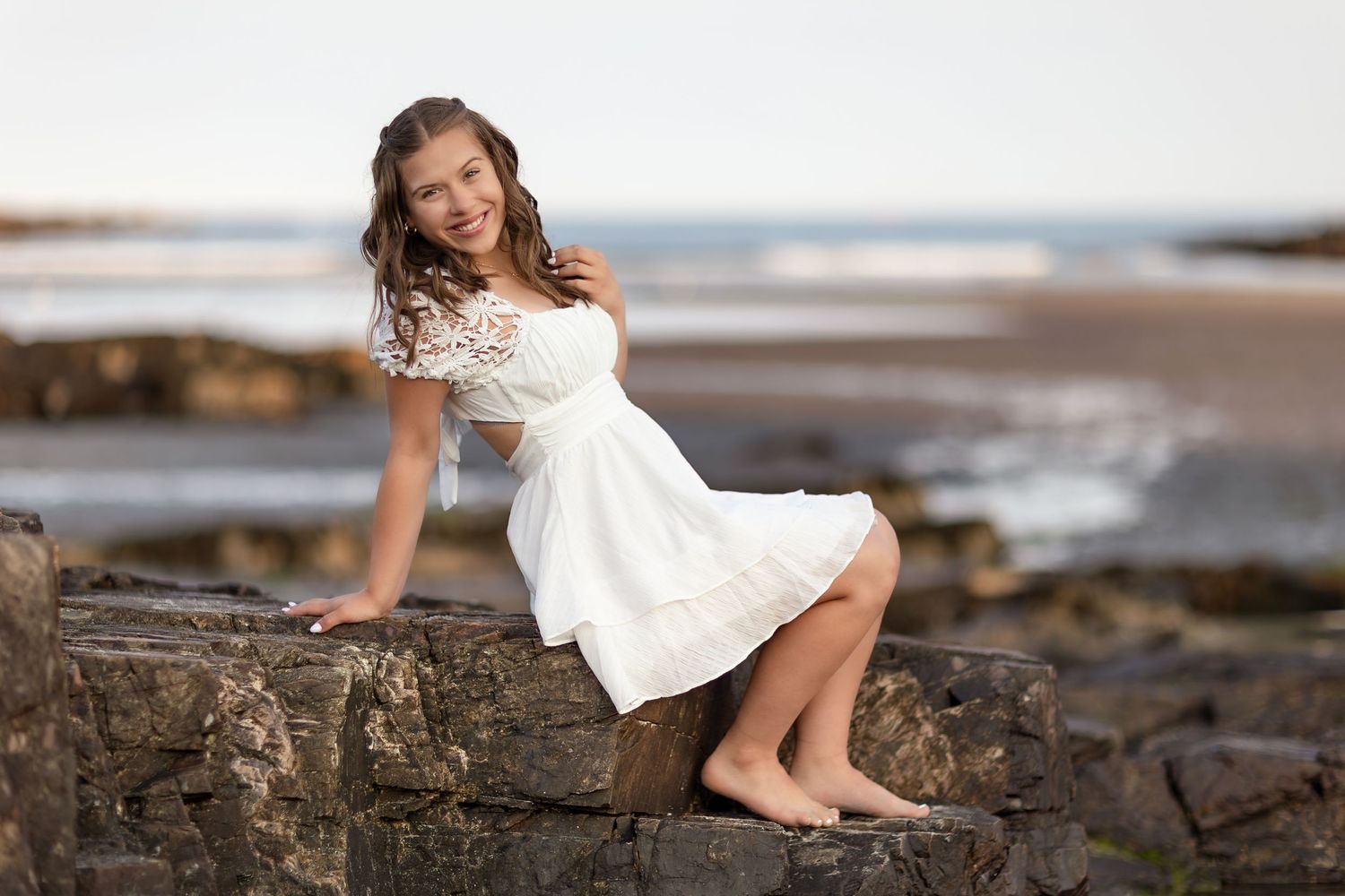 A white lace dress stands out against rocky coastal scenery at sunset.
