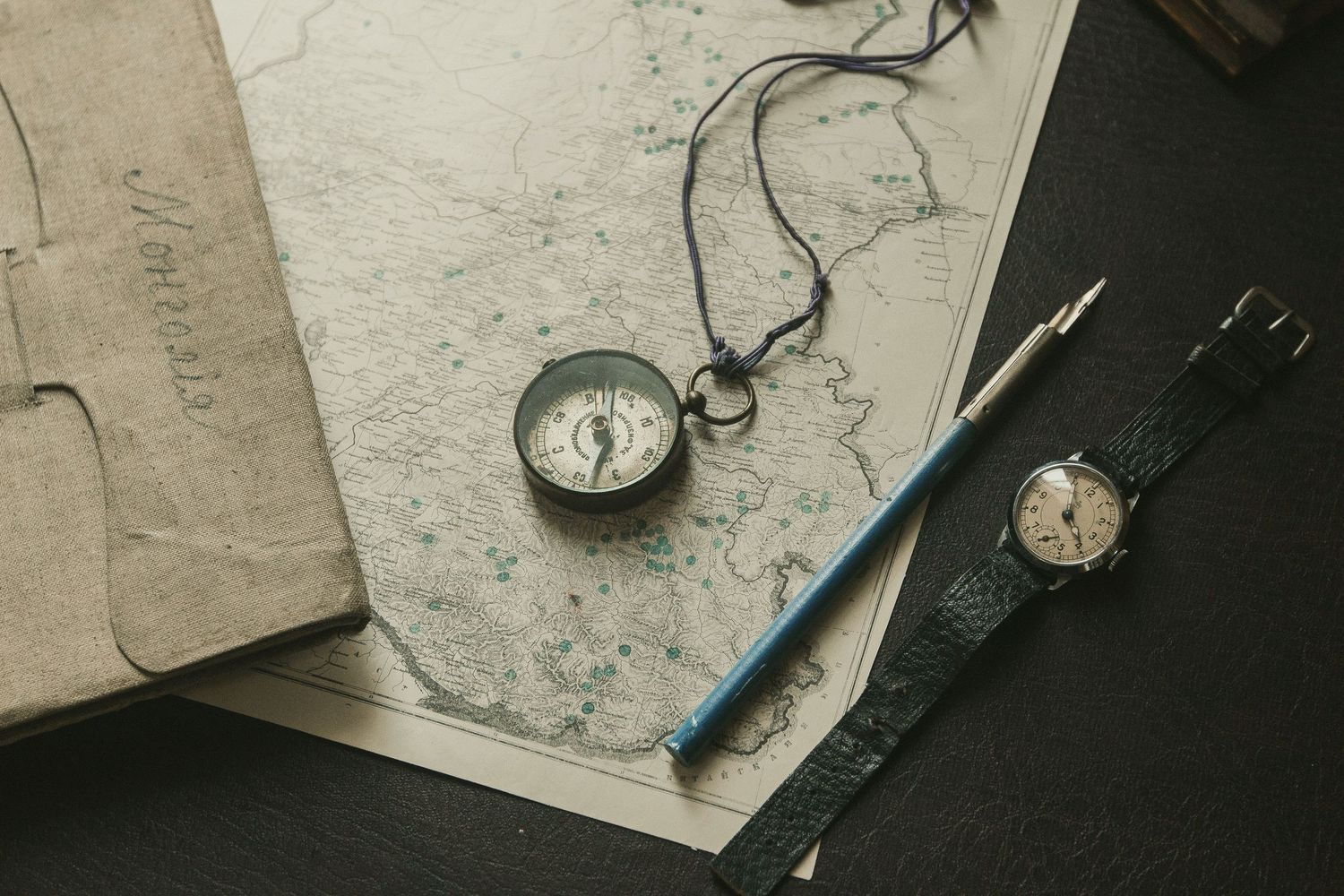 A vintage pocket watch with antique maps and documents on a weathered wooden surface creates a nostalgic composition.