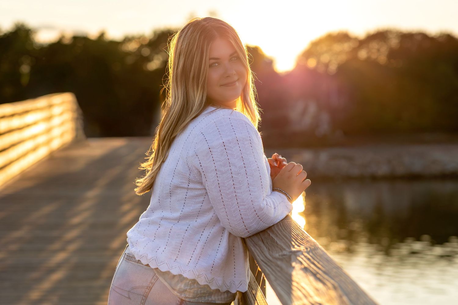 Ethereal golden hour photoshoot of a graduating senior in white lace dress by a serene lake at sunset.