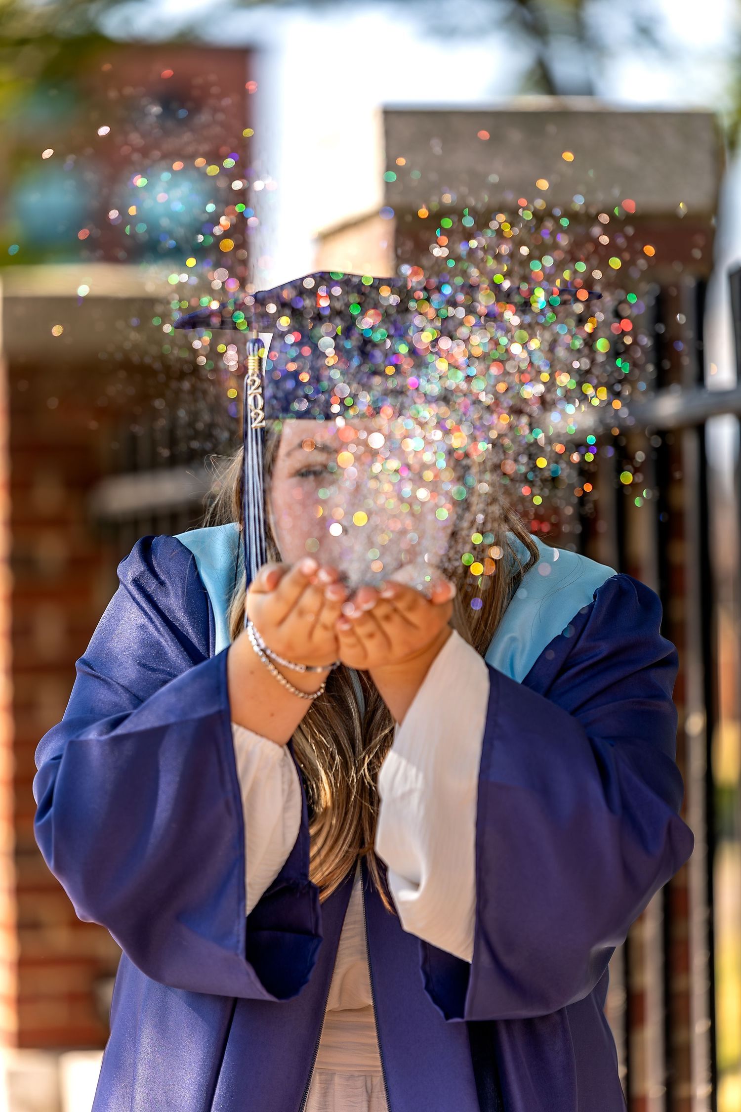 A person in a blue graduation gown throws colorful confetti into the air creating a festive celebratory moment.