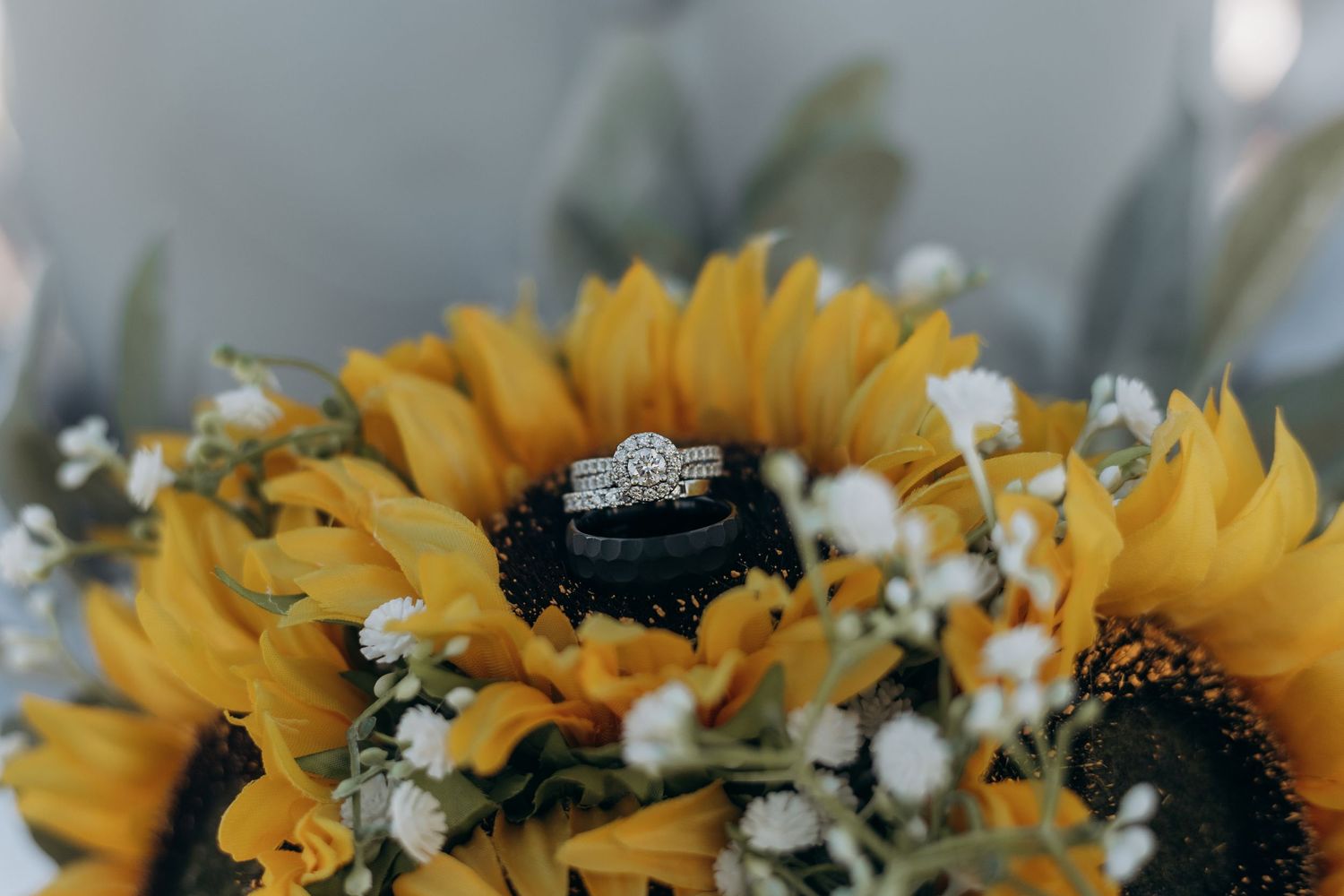 Wedding ring displayed on bright yellow sunflowers with small white baby's breath flowers in a bridal bouquet.