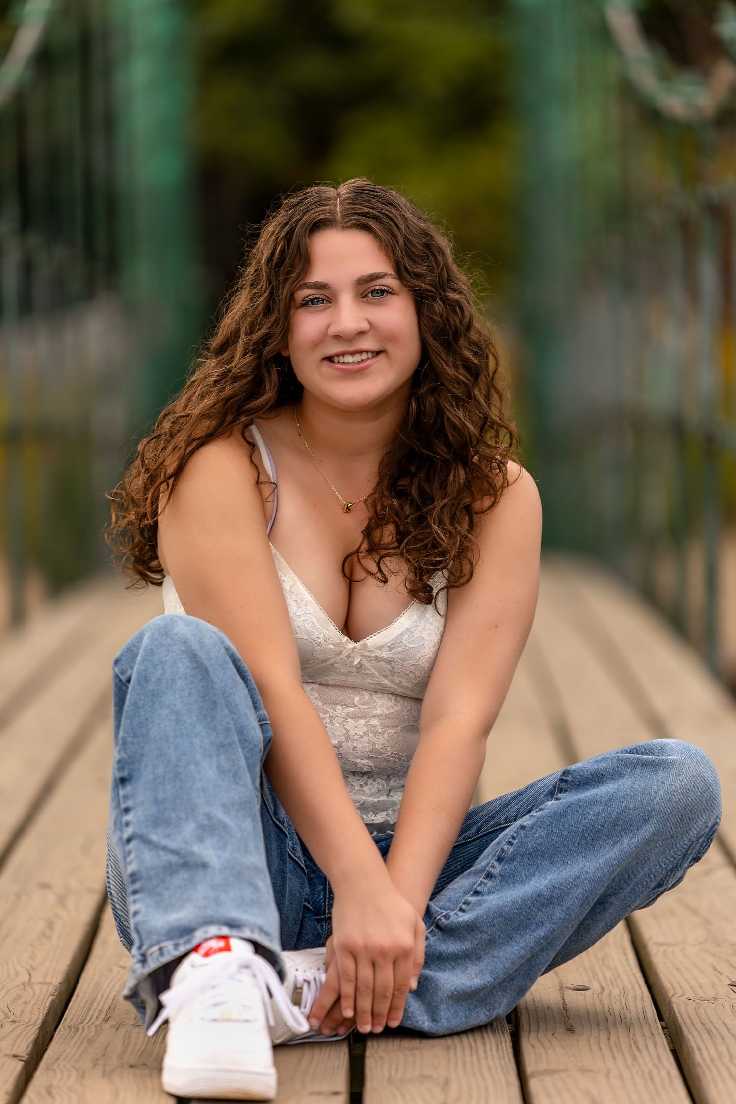 A graduating senior portrait series on wooden deck boards featuring someone in jeans and a white top with curly hair.