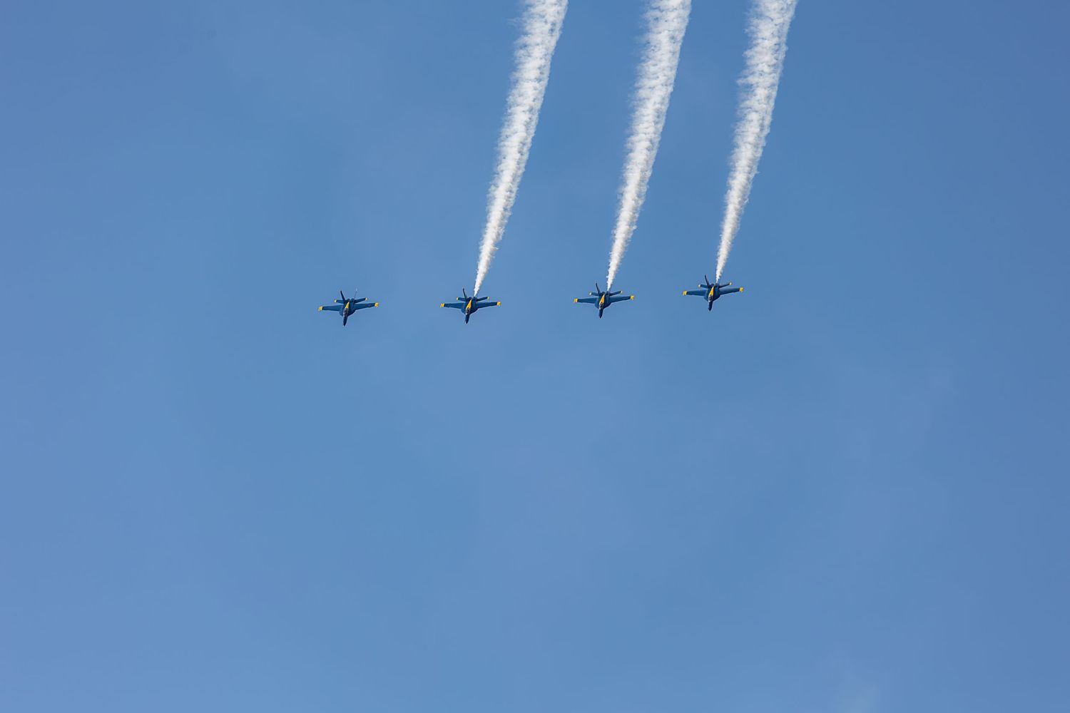 Three military jets fly in formation against a bright blue sky, creating a dramatic aerial display.