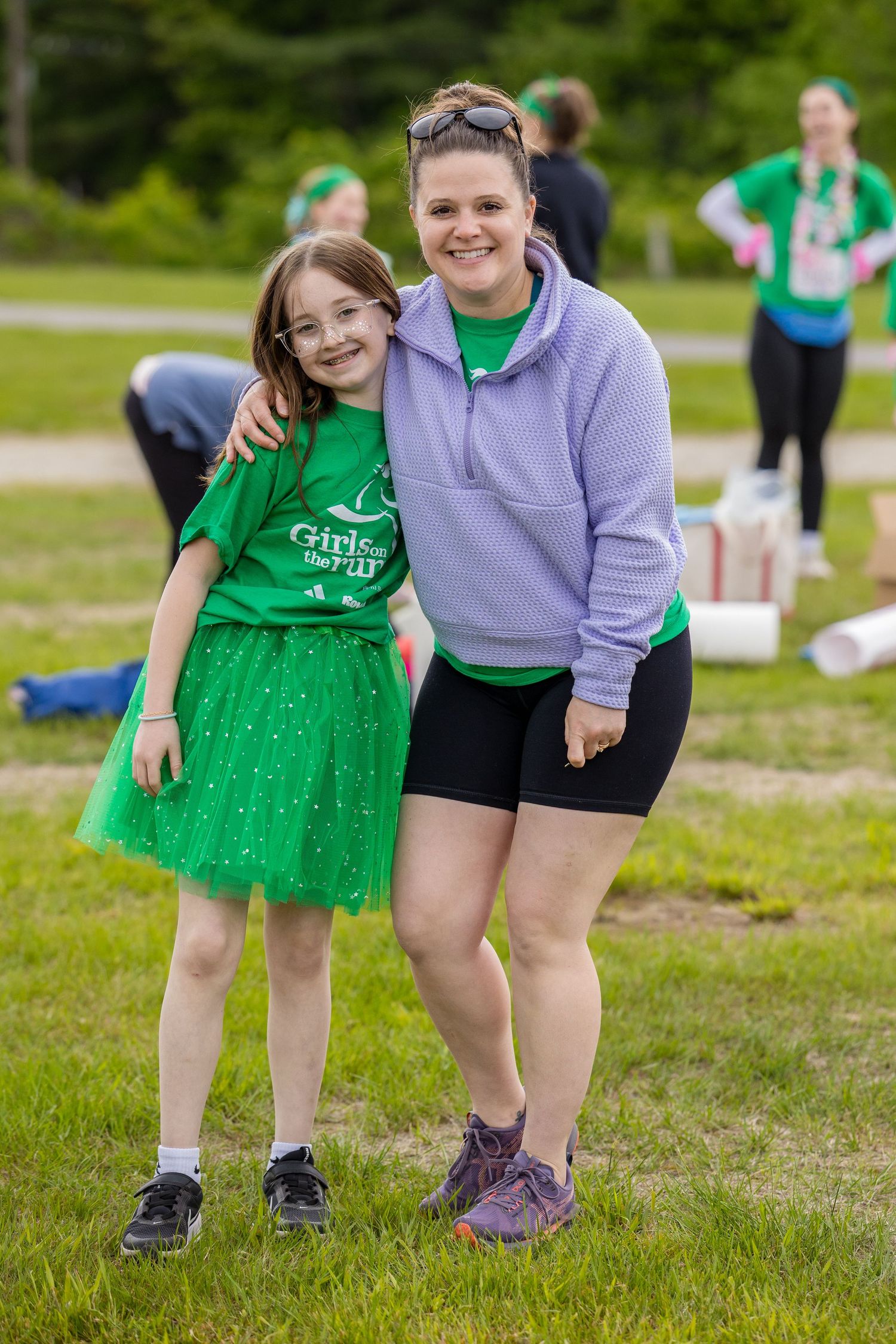 A woman and young girl in matching green outfits smile together at an outdoor Girls on the Run event.