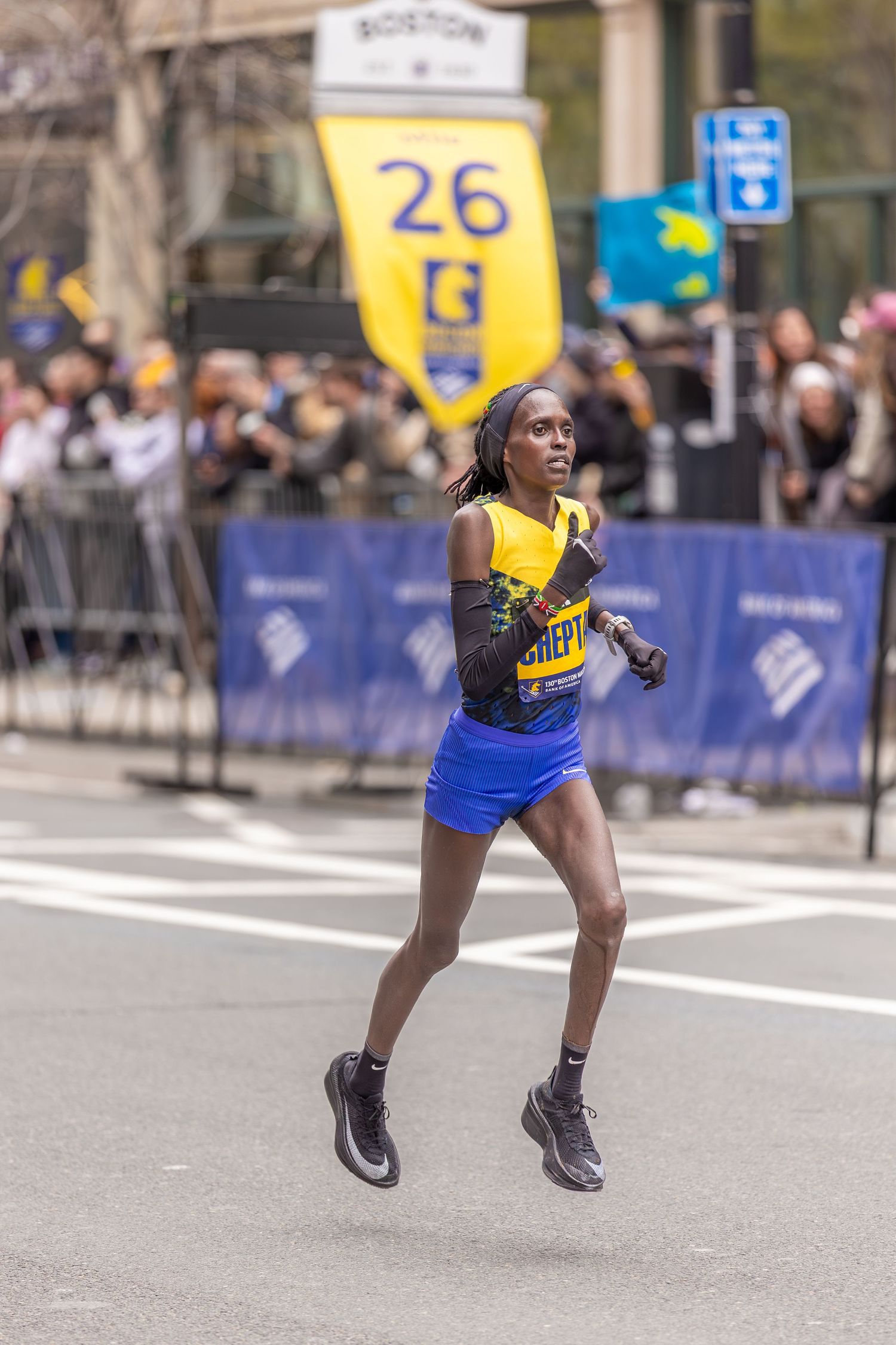Female runner in yellow top and blue shorts competing at mile 26 of the Boston Marathon.
