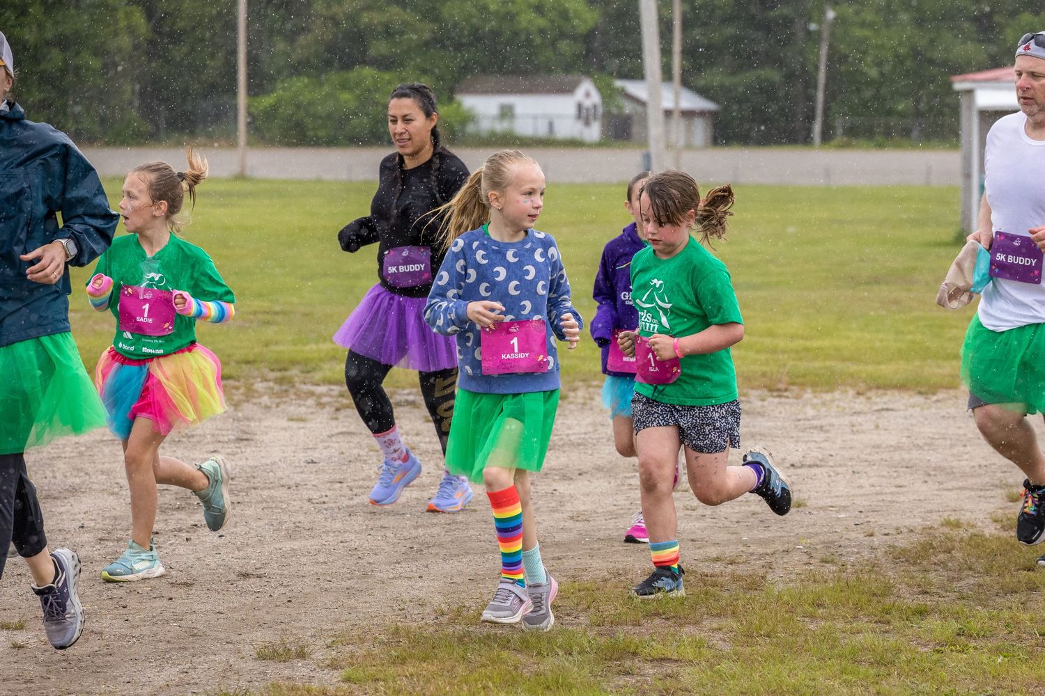 Girls in colorful tutus and rainbow outfits running in a fun kids charity race outdoors.