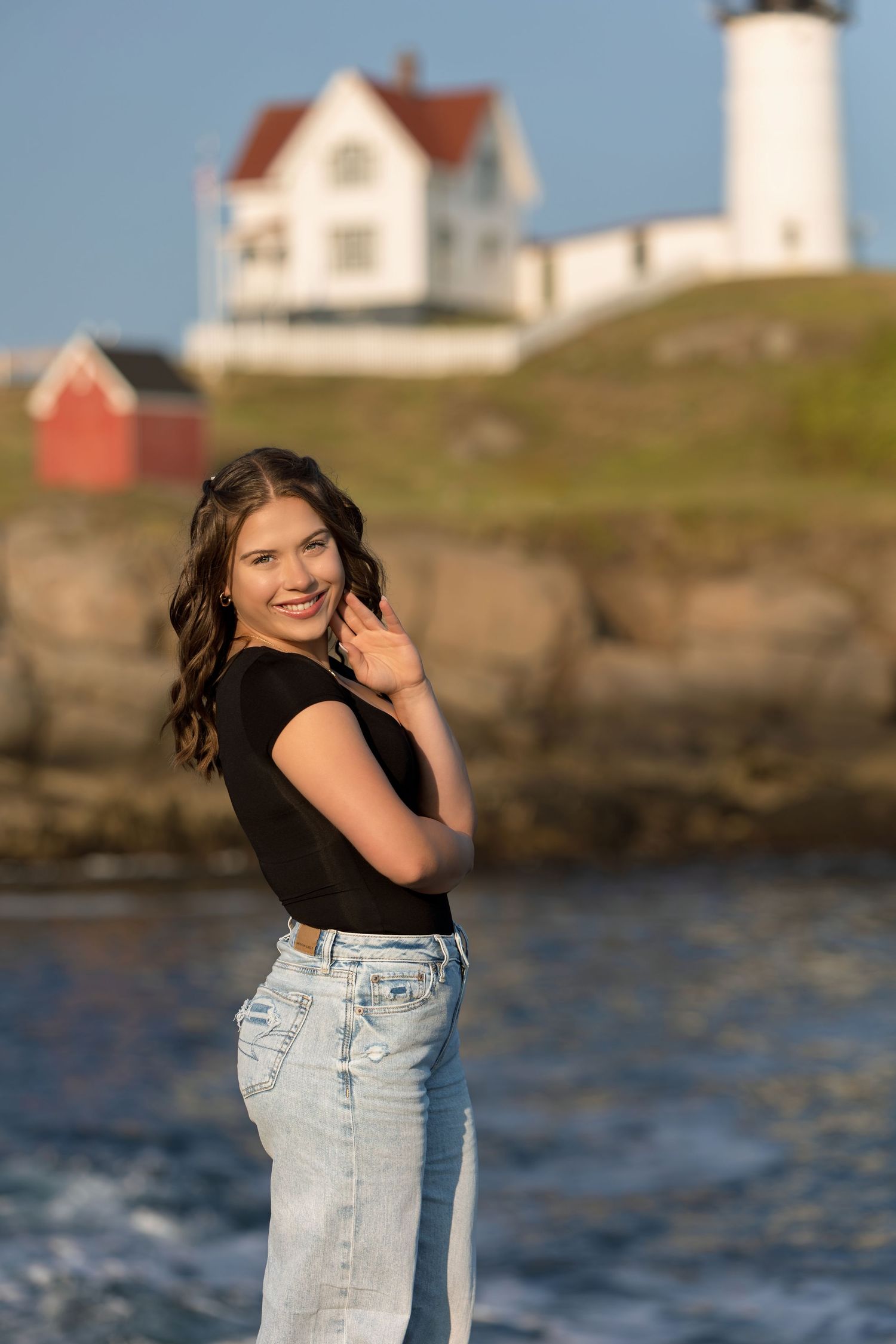 A casual pose in front of the Nubble Lighthouse in Maine wearing denim and black top.
