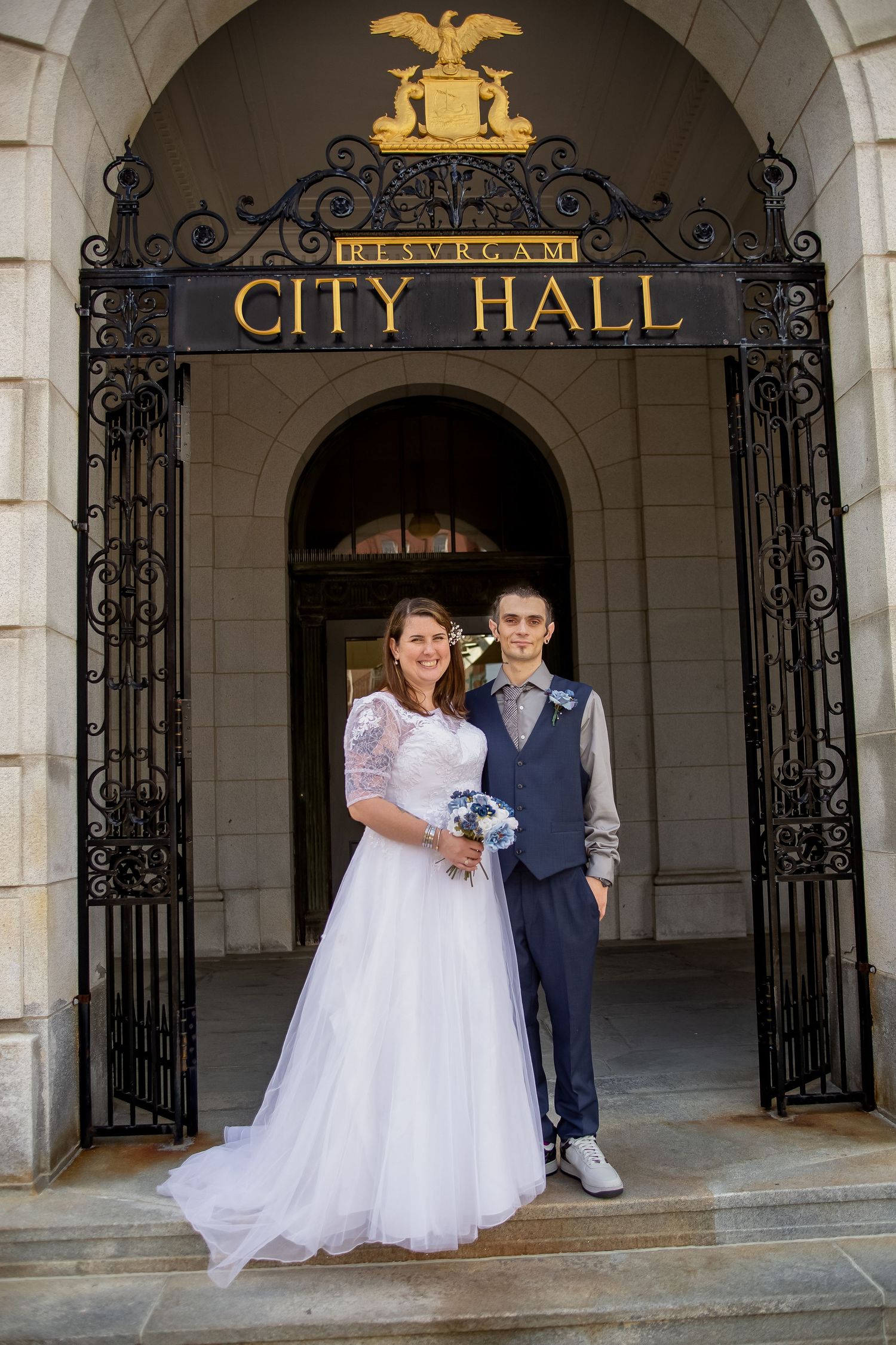 Wedding couple poses together at City Hall entrance with ornate iron gates and architectural details.