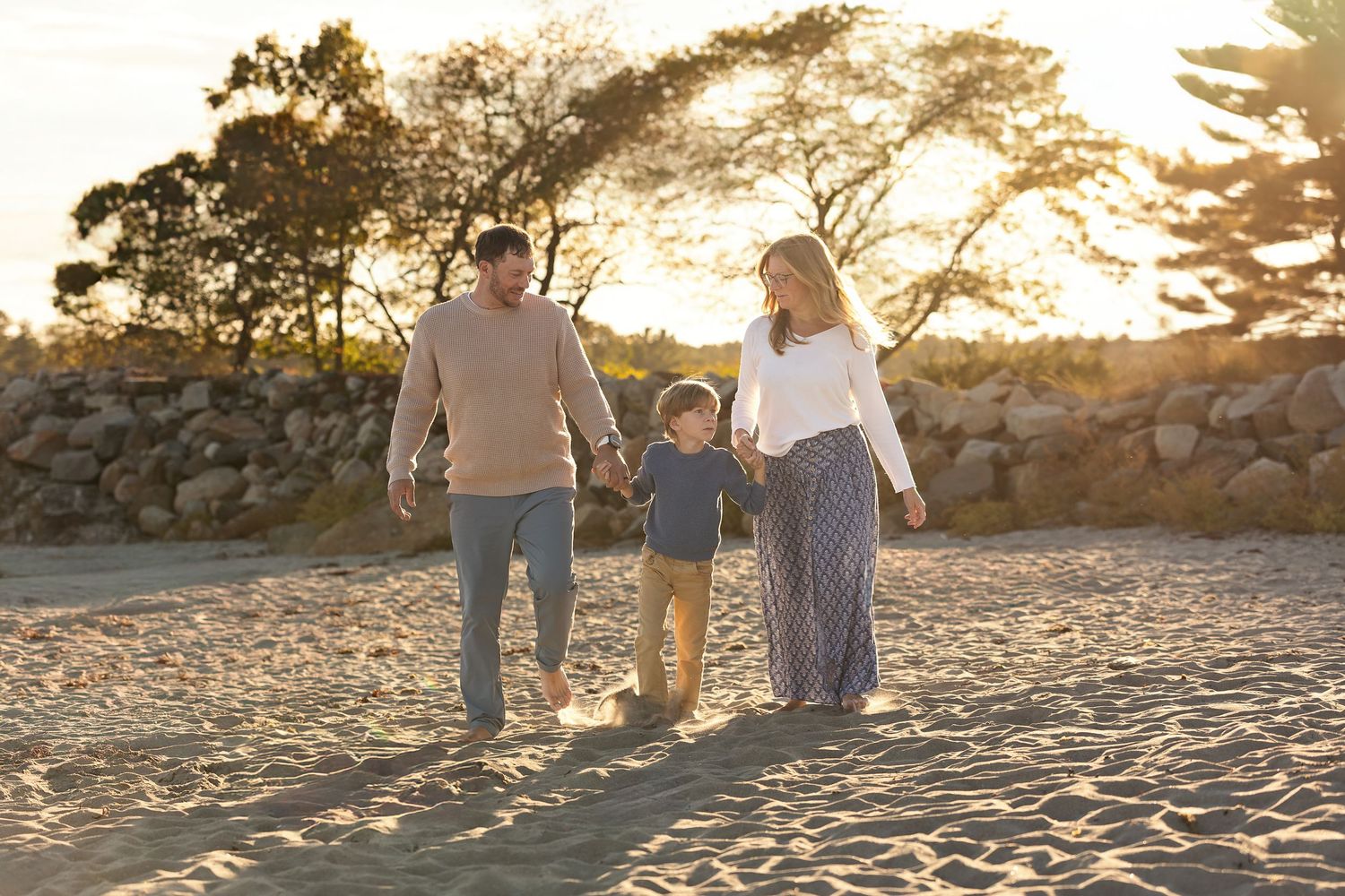 A family walks together on a beach at sunset casting long shadows on the golden sand.