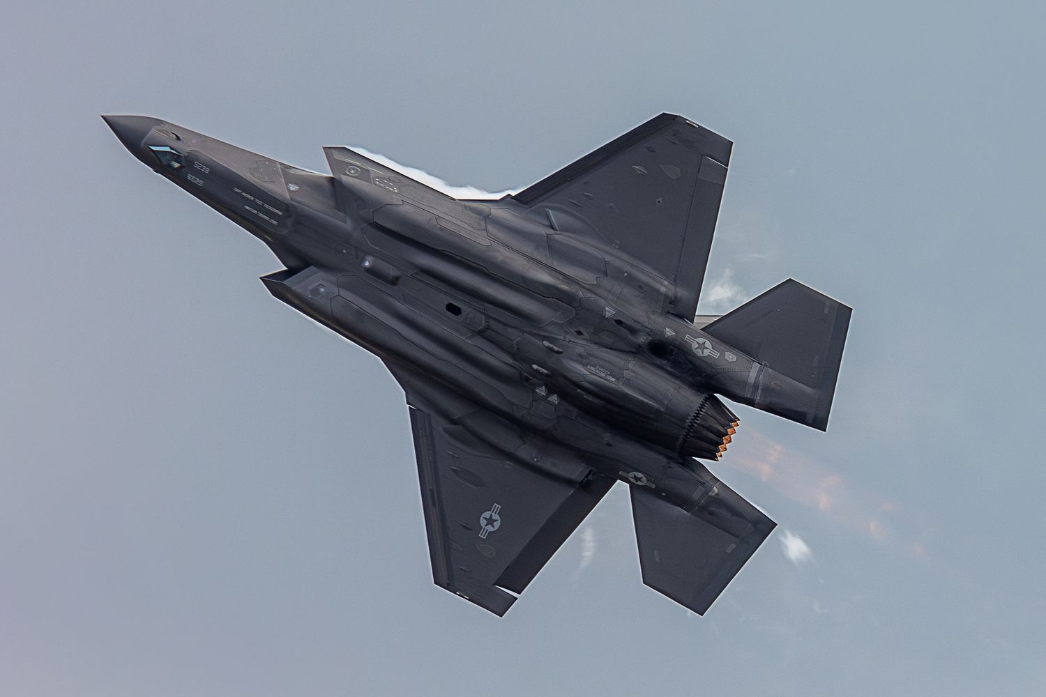 F-35 Lightning II fighter jet performs a high-speed banking maneuver against a cloudy sky backdrop.