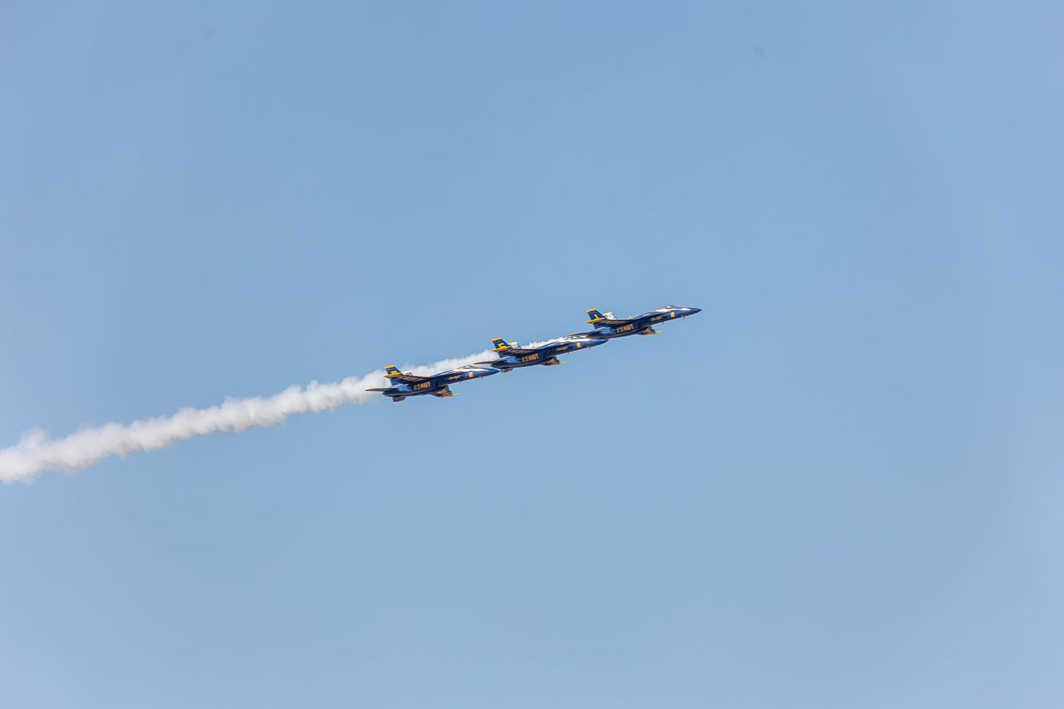 Military fighter jets fly in formation leaving white smoke trails against a bright blue sky during an air show display.
