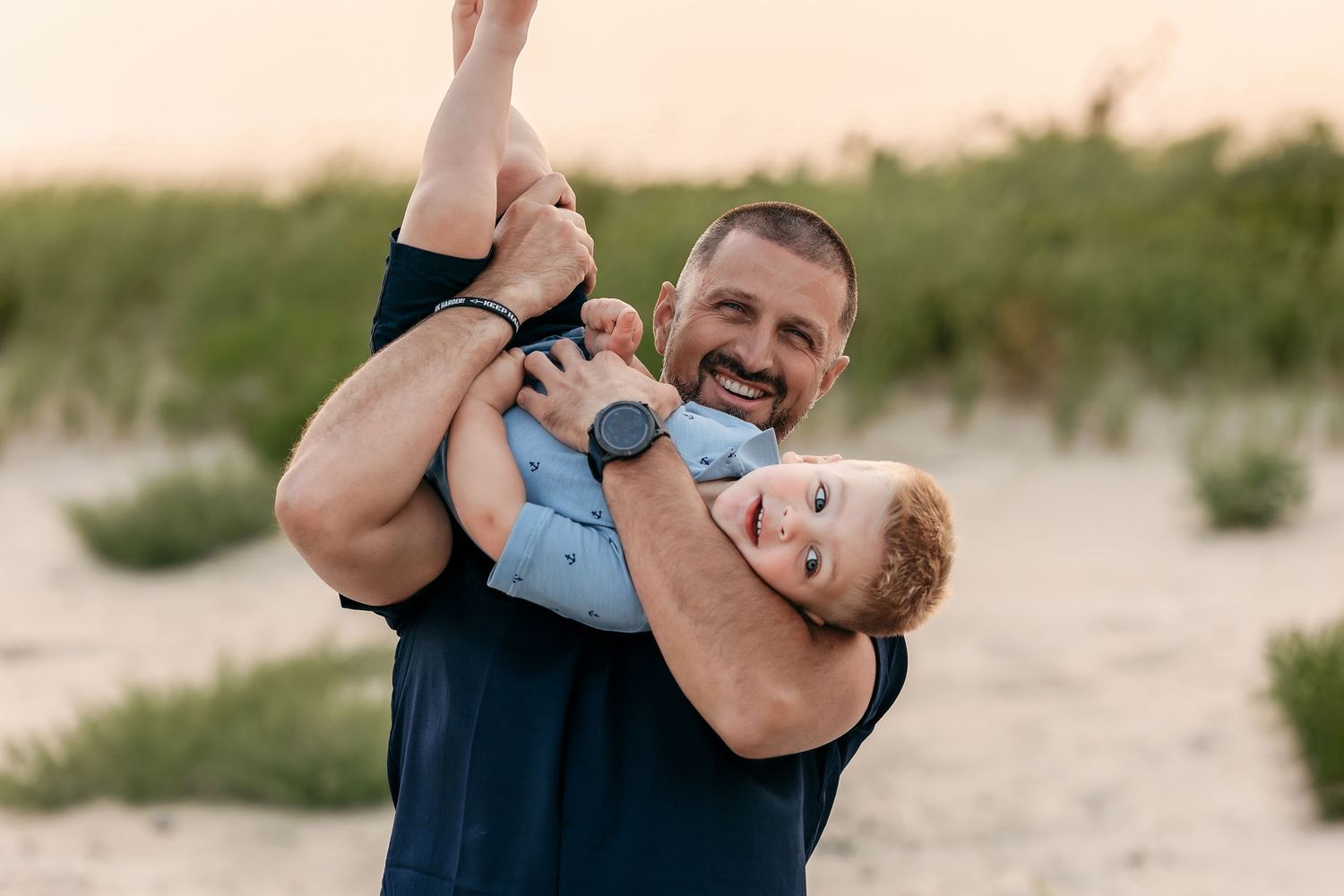 A person embraces and kisses a small child on a beach at sunset, creating a tender silhouetted moment.