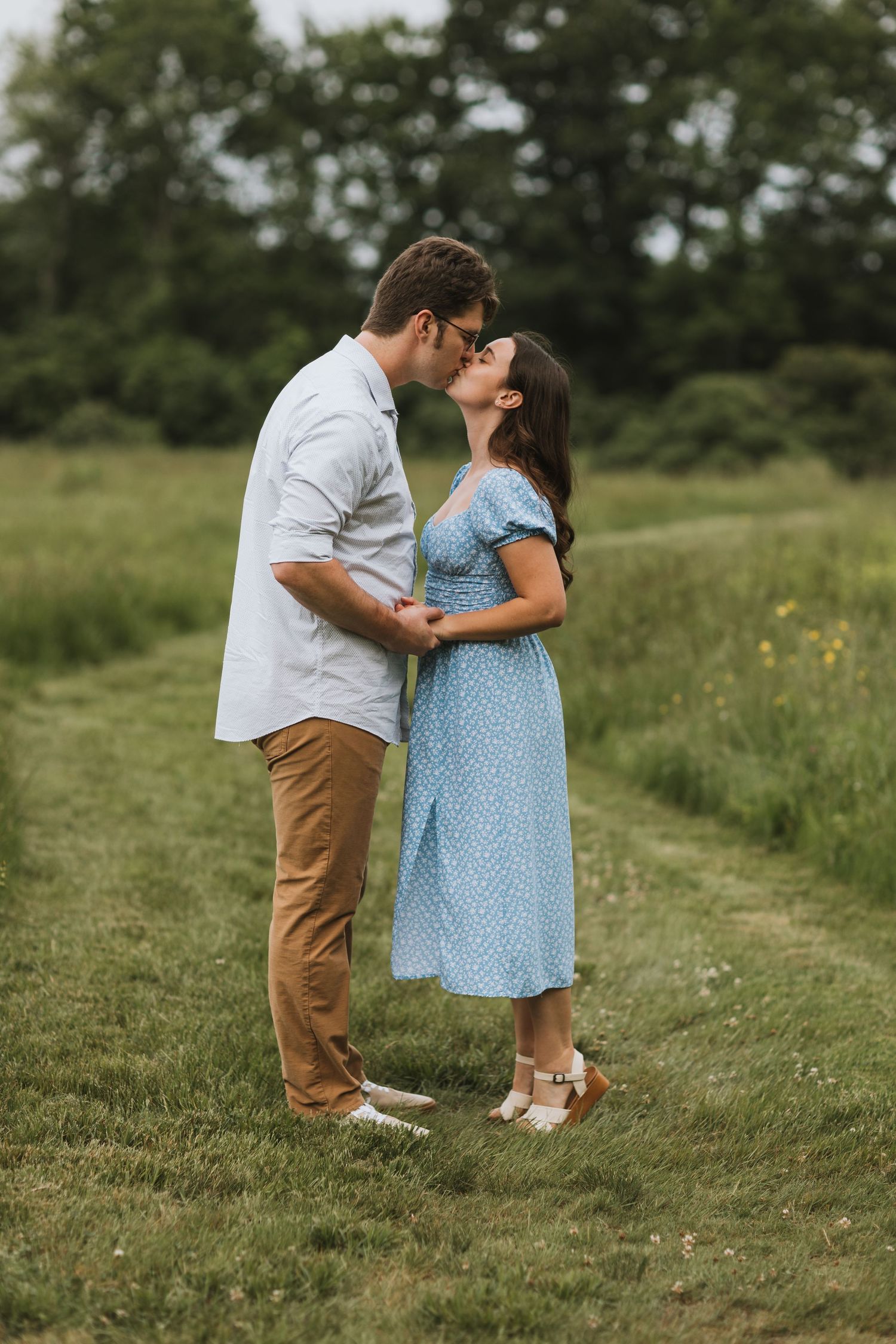 A romantic couple shares a tender moment on a grassy path surrounded by lush greenery on a summer day for their engagement session.