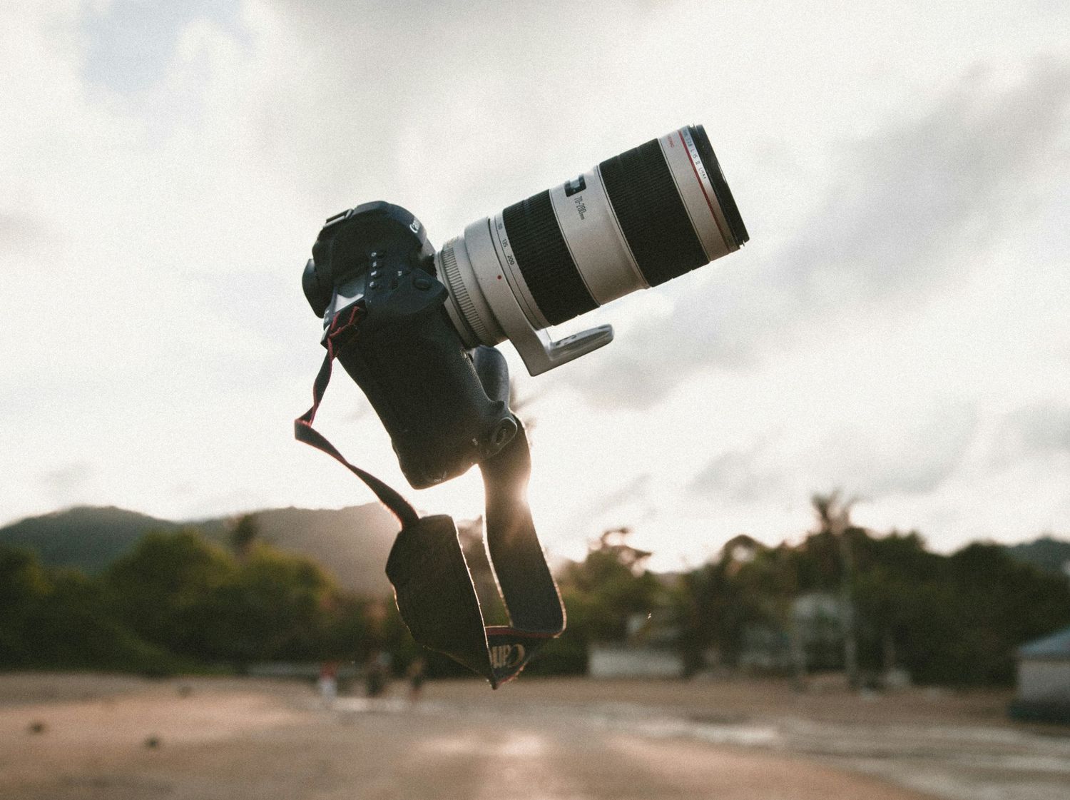 A large DSLR camera with telephoto lens appears to float against a cloudy sky at sunset.