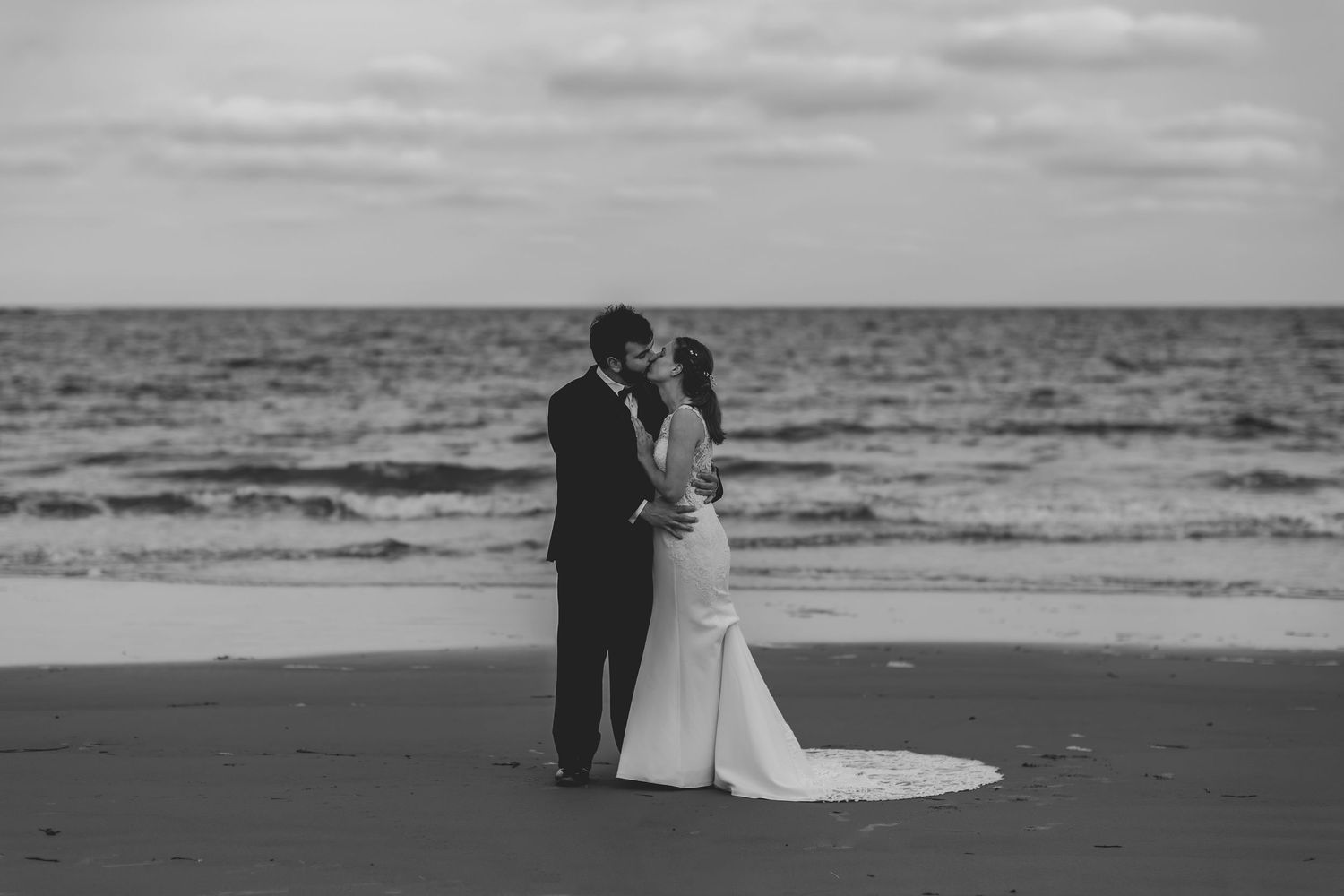 A couple shares a romantic moment on a beach at sunset, with the ocean waves gently rolling in the background.