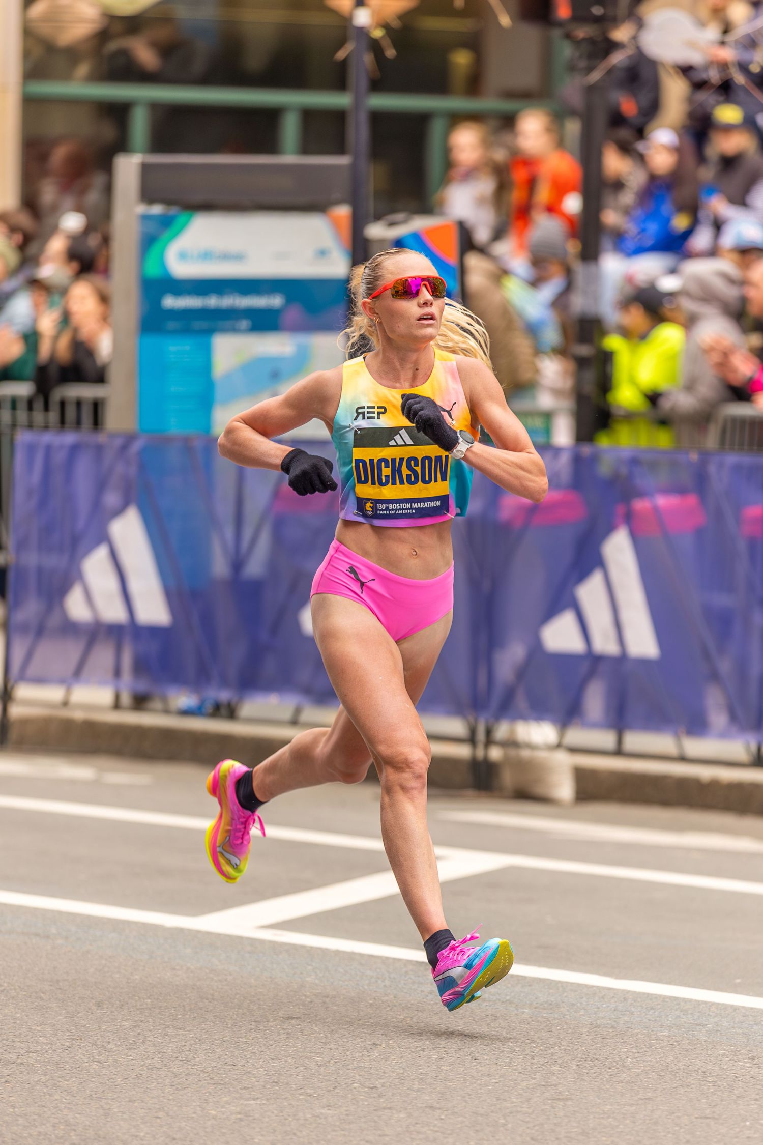 Runner Dickson competing in the Boston Marathon wearing yellow and pink athletic gear and colorful sneakers.