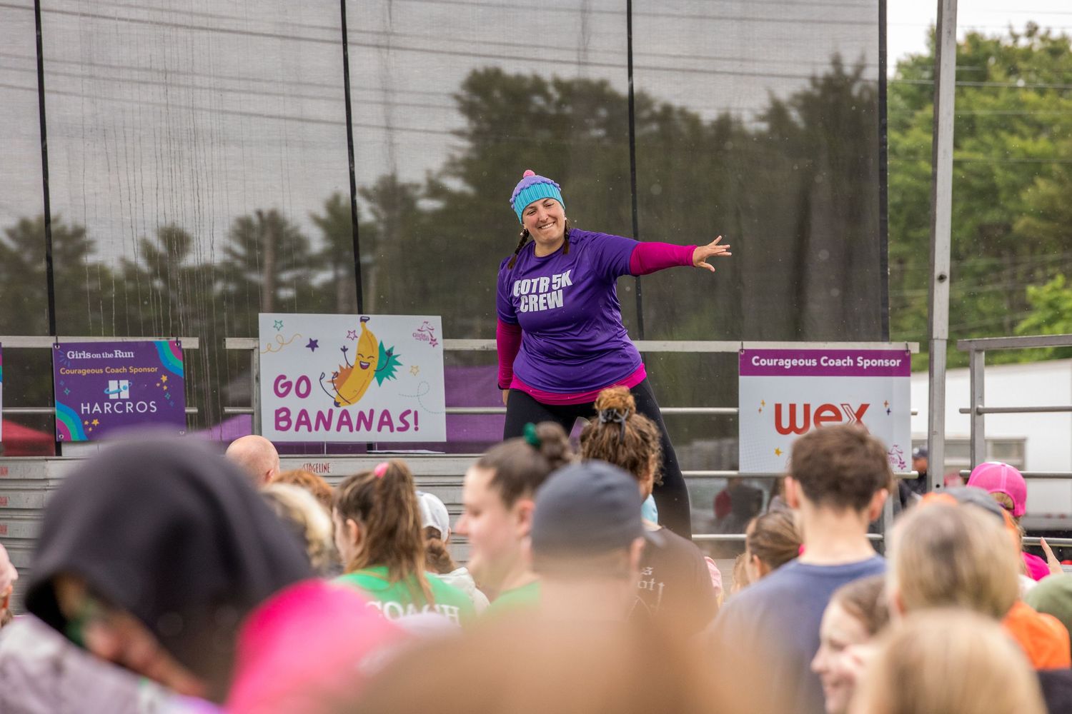 Energetic fitness instructor leads outdoor group exercise event with crowd, Go Bananas sign visible in background.
