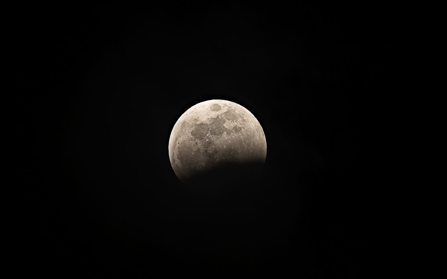Partial lunar eclipse against a dark night sky, showing the moon partially shadowed by Earth's umbra.