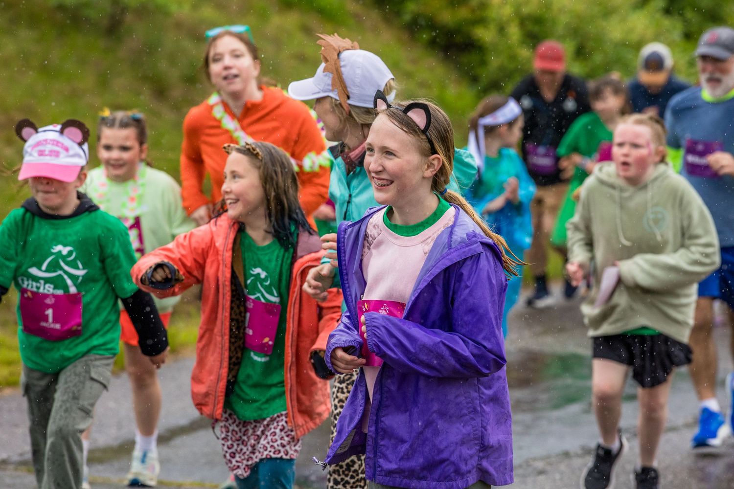 Children smiling and running together in a colorful fun run race event outdoors on a paved road.