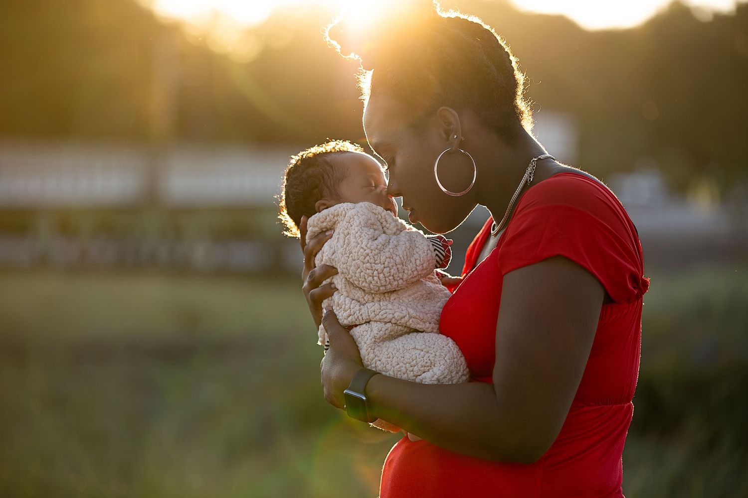 A parent holds a small baby while standing outdoors during golden hour sunset.