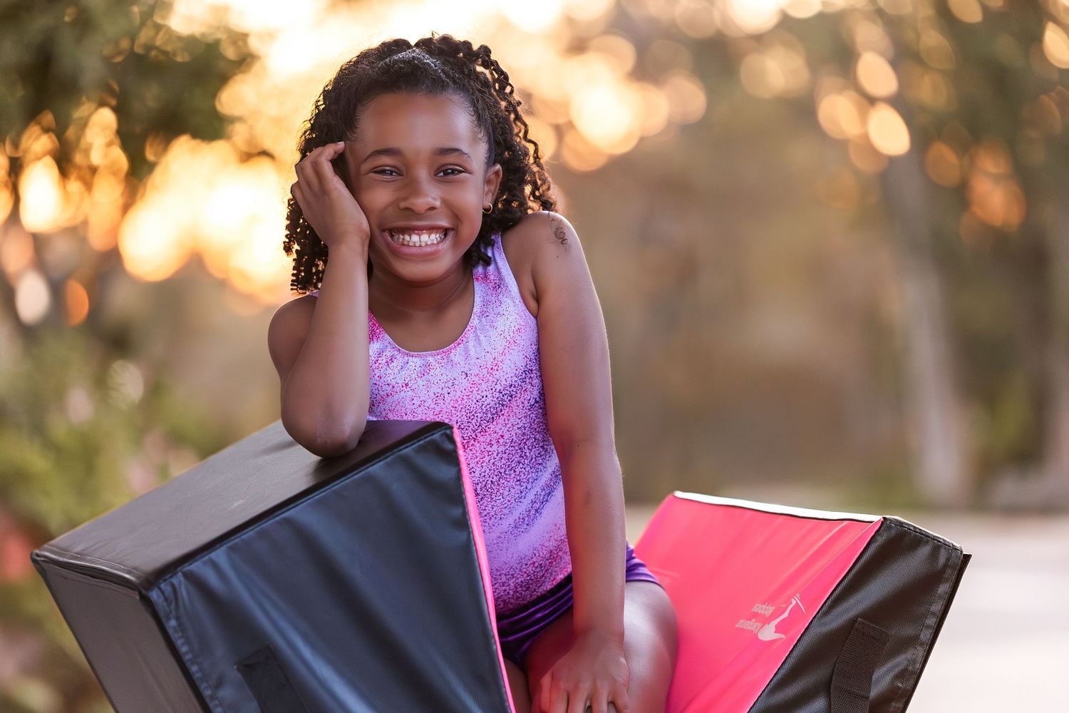 A child sits on a red yoga mat outdoors during a golden sunset, creating a joyful moment in nature.