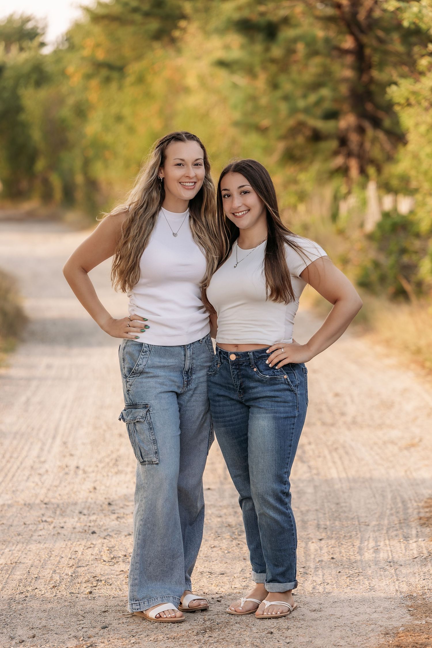 Two friends in white tops and jeans posing on rural dirt road.