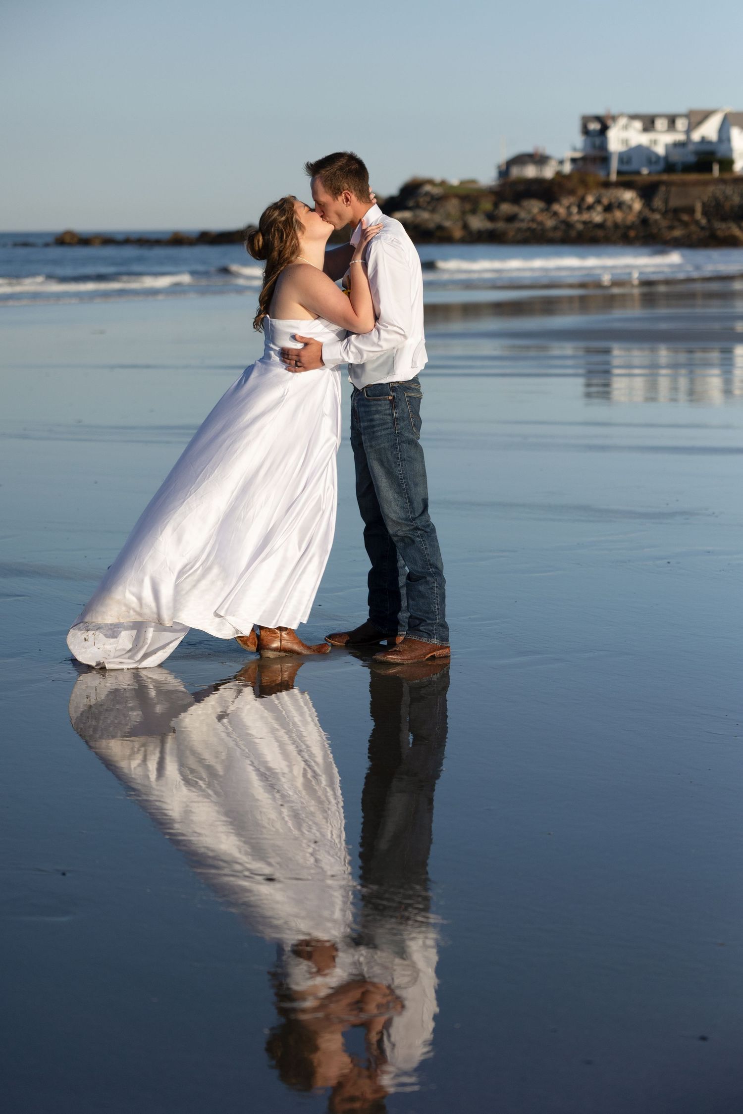 A couple shares a romantic moment on a reflective beach at sunset with their image mirrored in the wet sand.